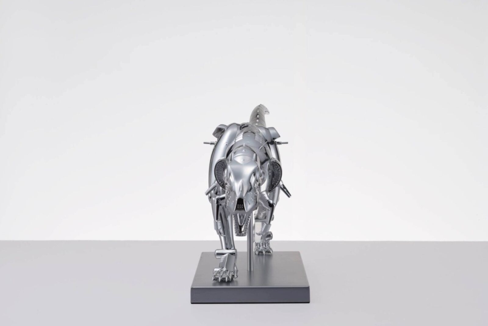 A metal model of a t-rex on a white surface.