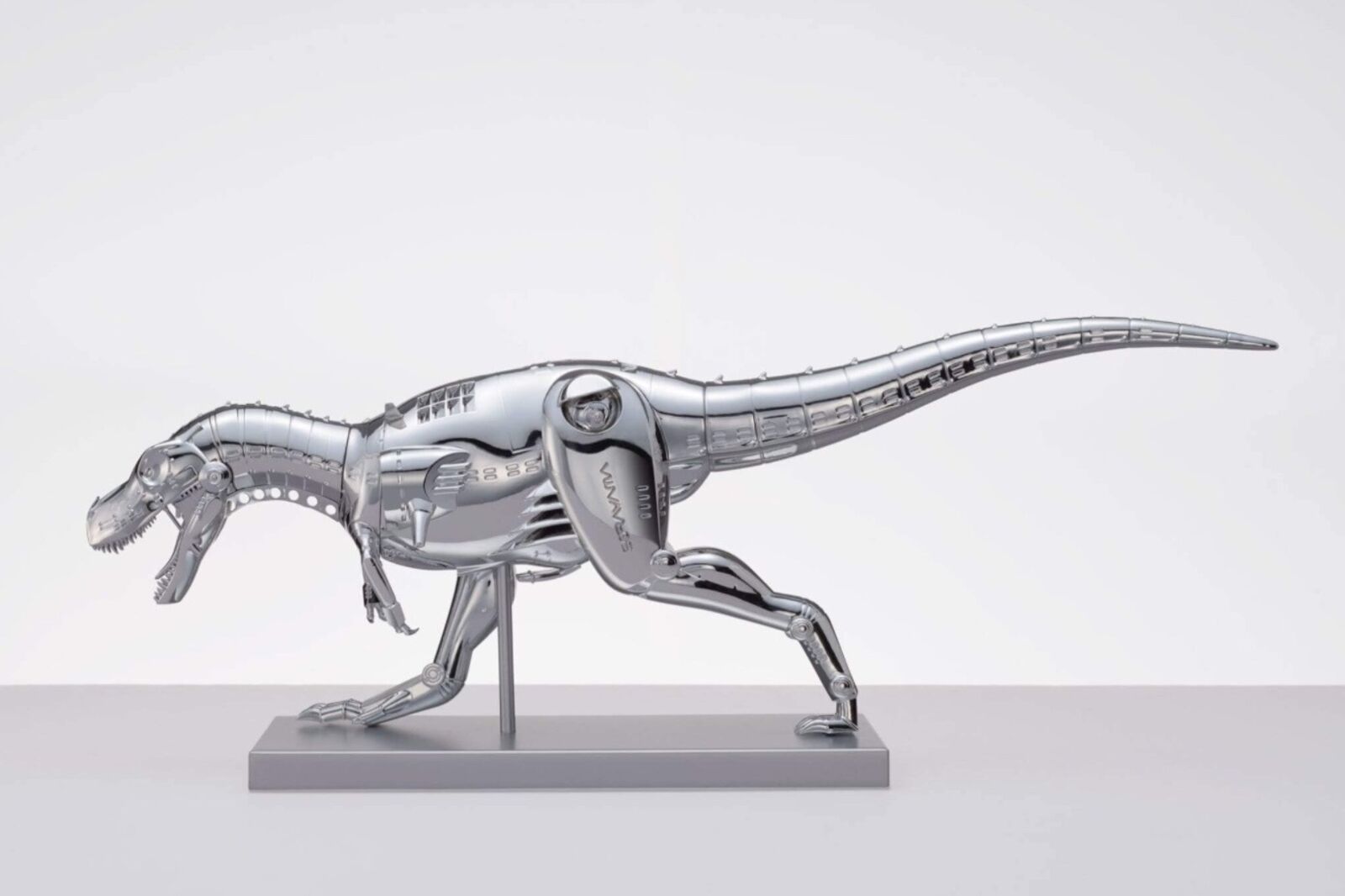 A metal model of a t-rex on a white surface.