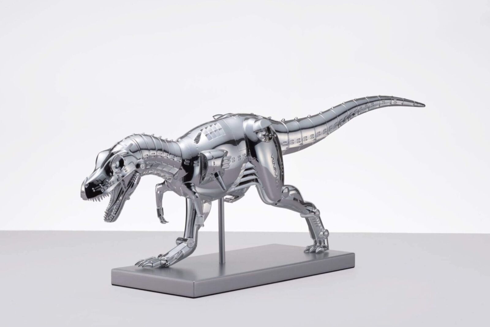 A metal model of a t-rex on a white surface.