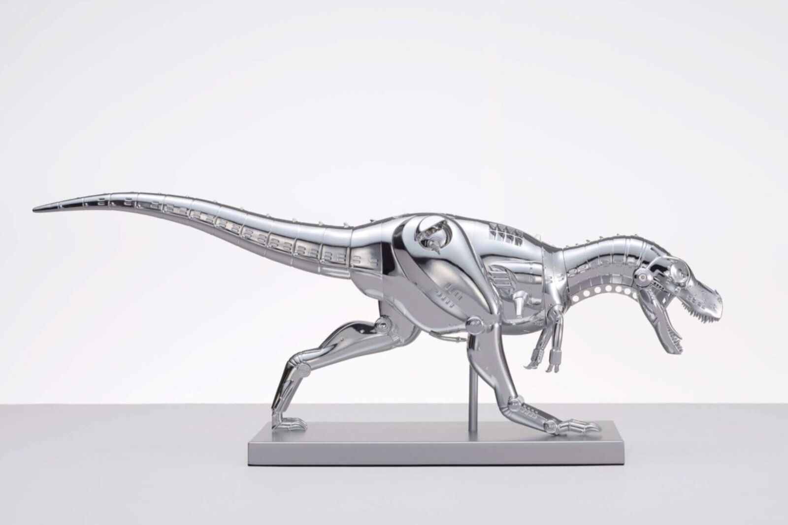 A metal model of a t-rex on a white surface.