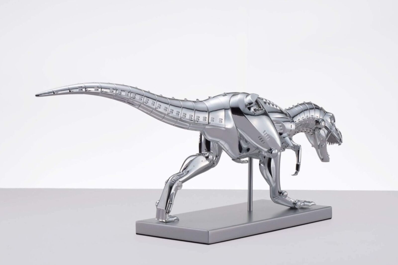 A metal model of a t-rex on a white surface.