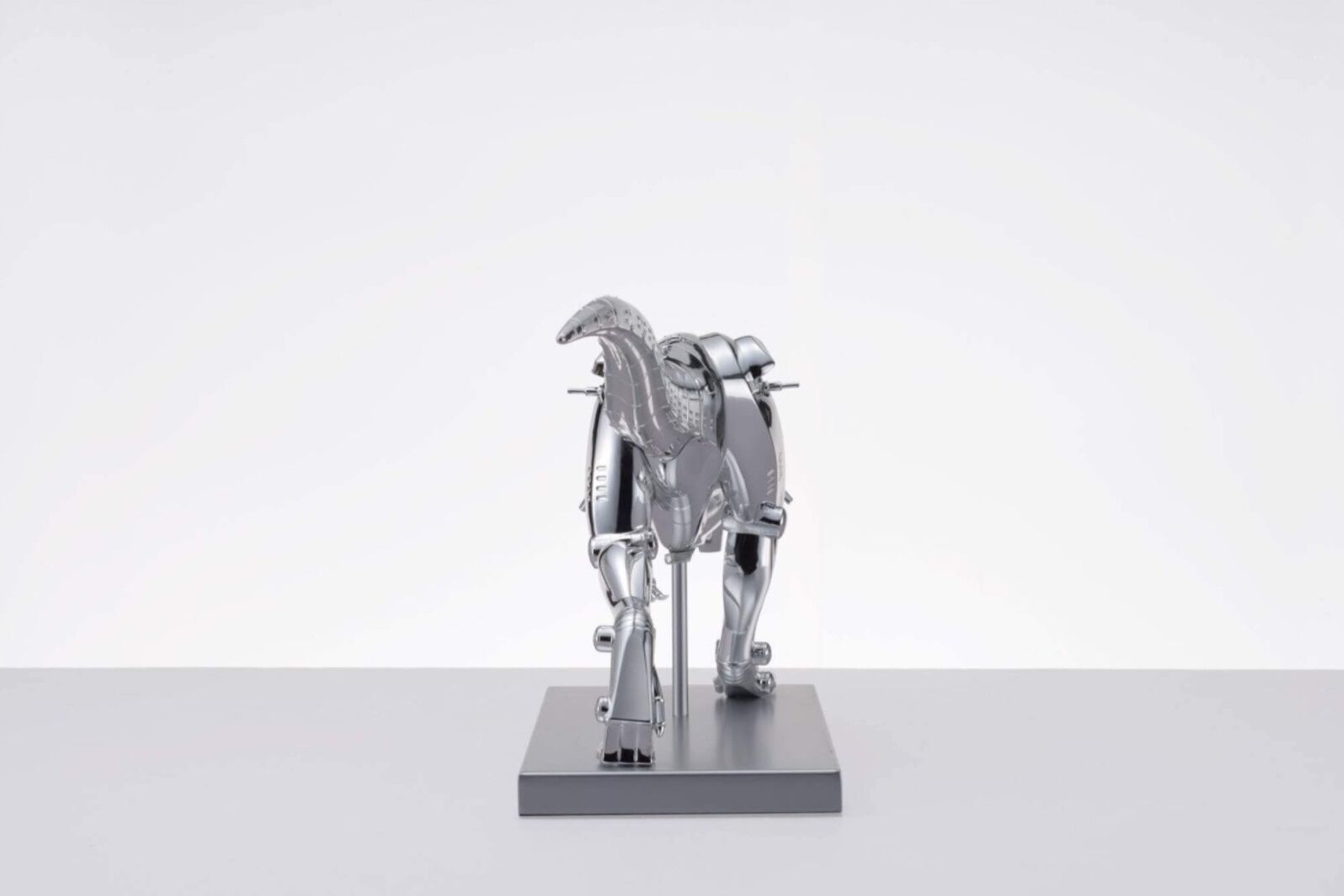 A metal model of a t-rex on a white surface.