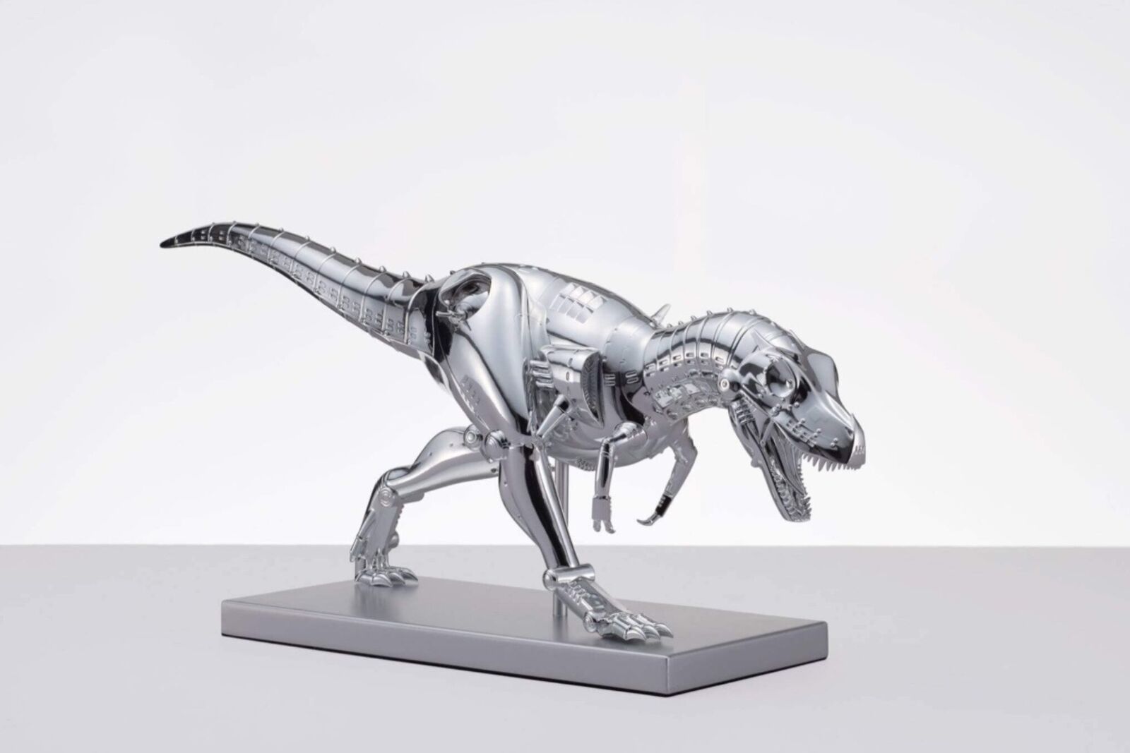 A metal model of a t-rex on a white surface.