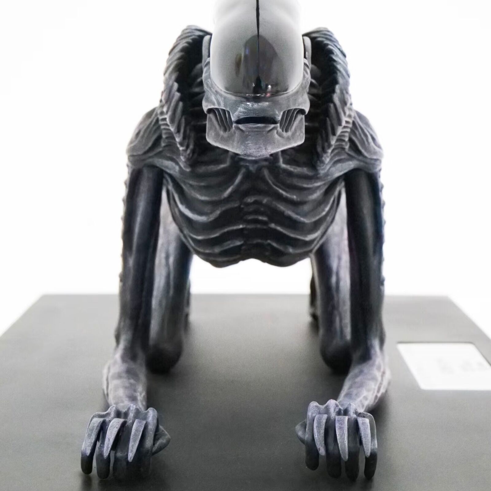 A statue of an alien with a long tail on a black base.