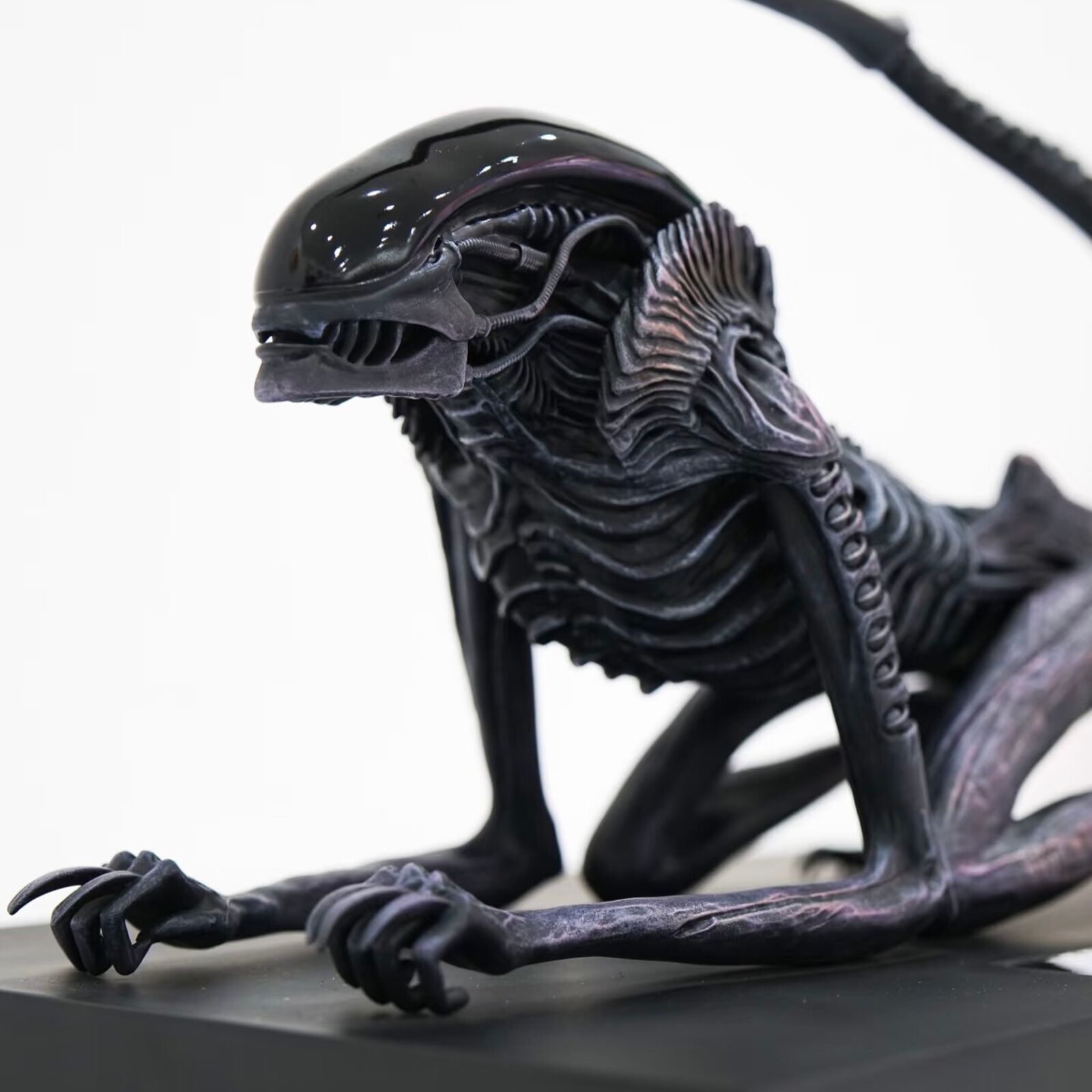 A statue of an alien with a long tail on a black base.