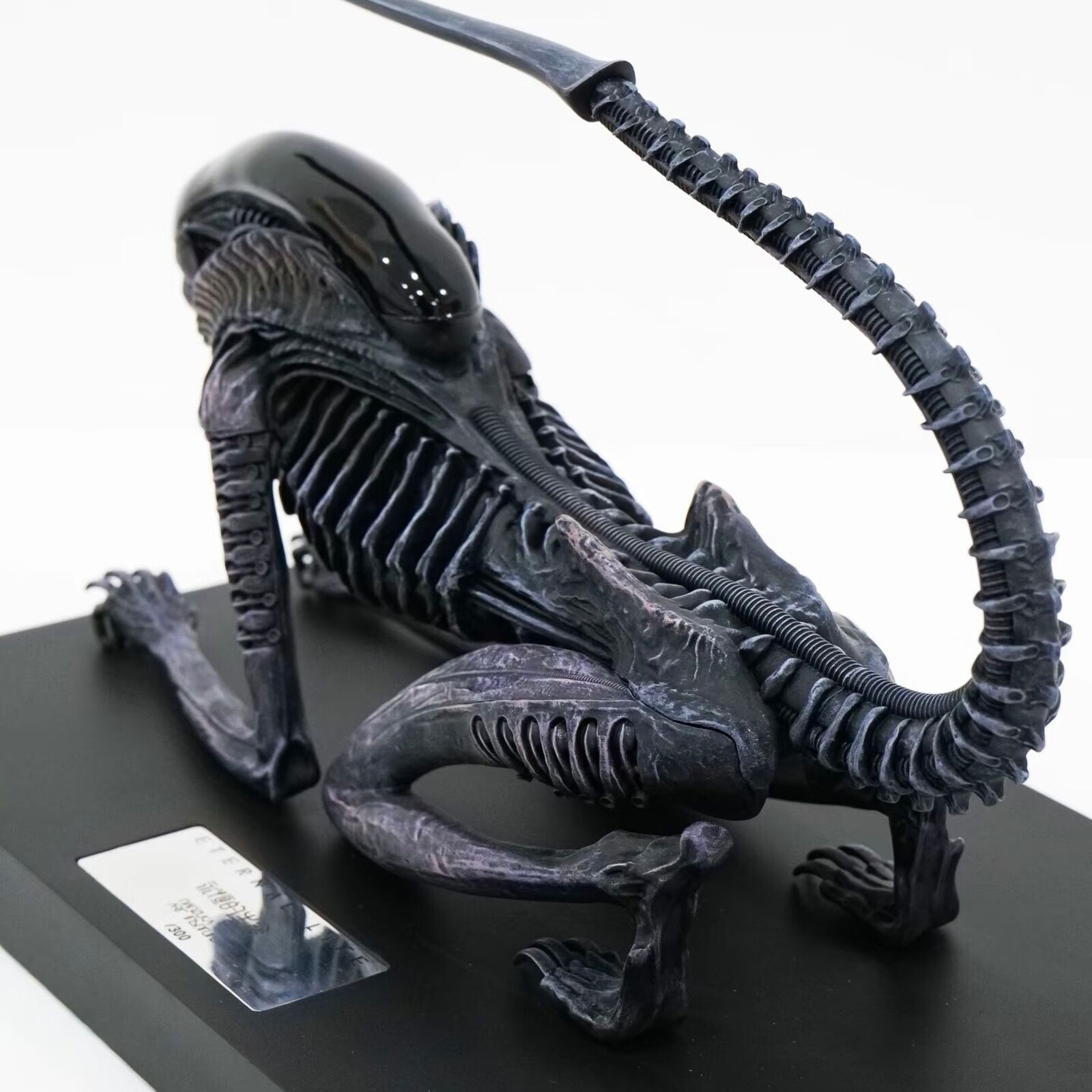 A statue of an alien with a long tail on a black base.