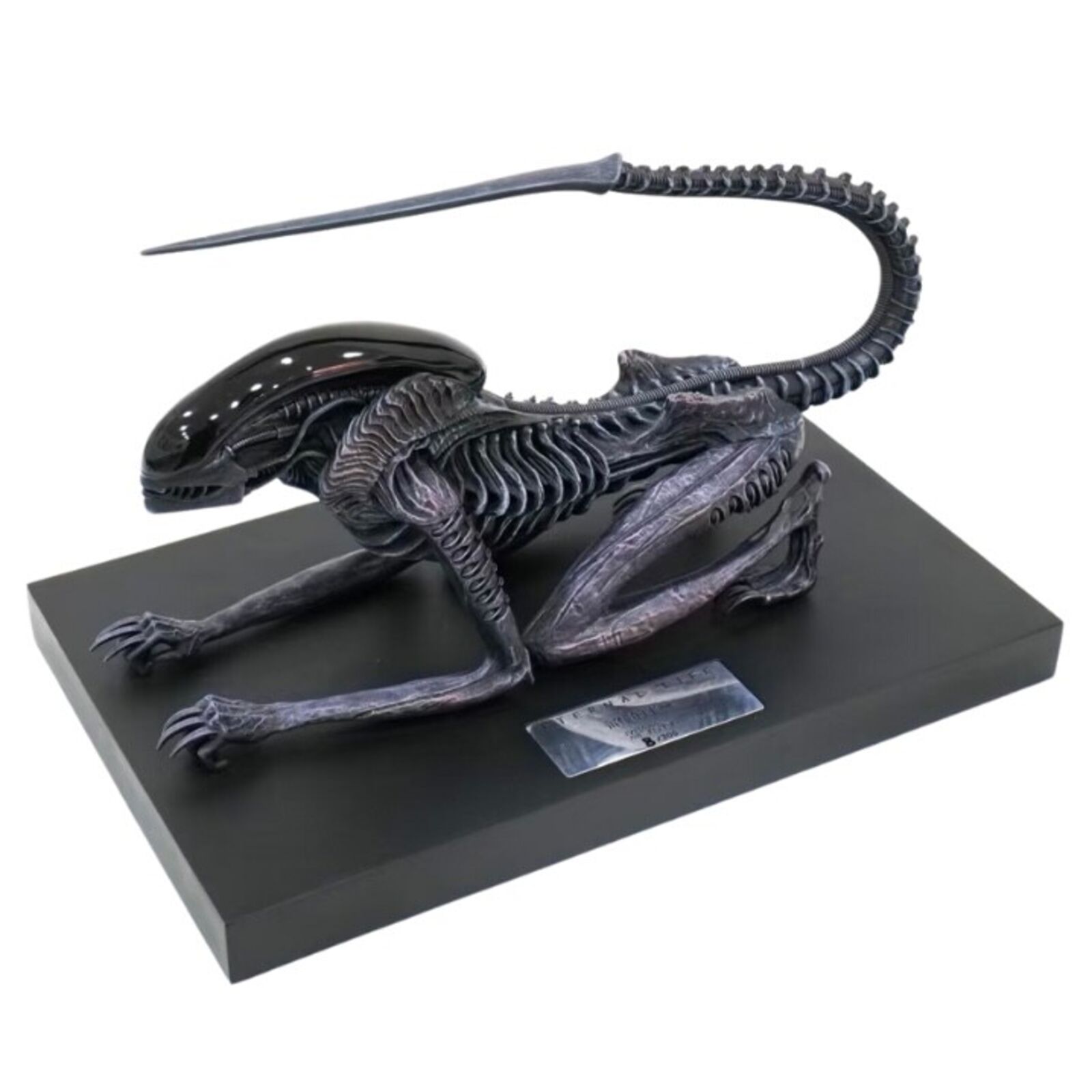 A statue of an alien with a long tail on a black base.