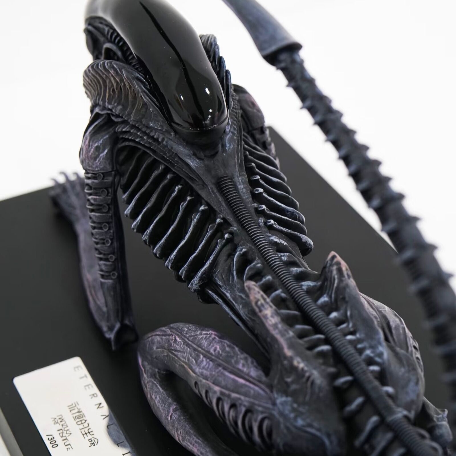 A statue of an alien with a long tail on a black base.