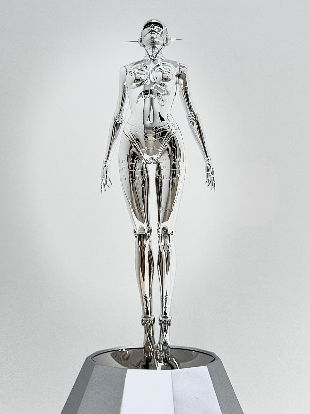 A silver metal sculpture of a woman standing on a pedestal.
