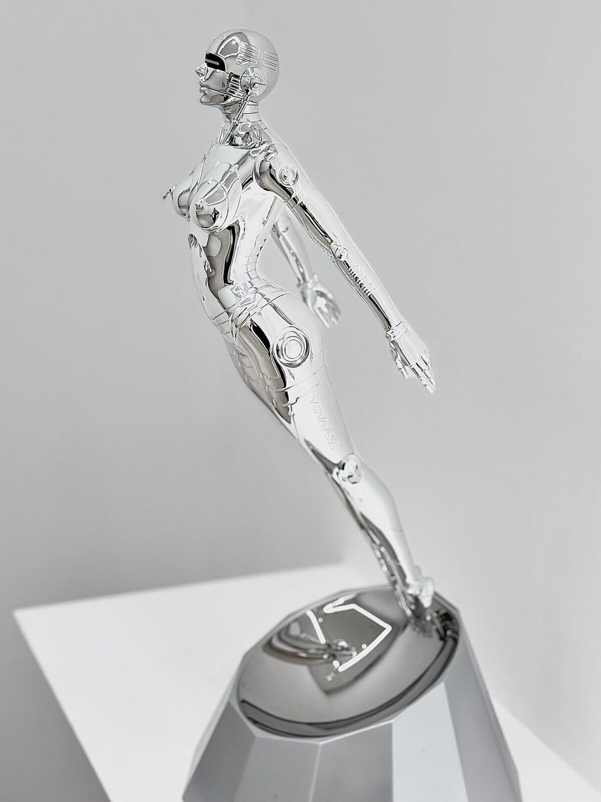 A silver metal sculpture of a woman standing on a pedestal.