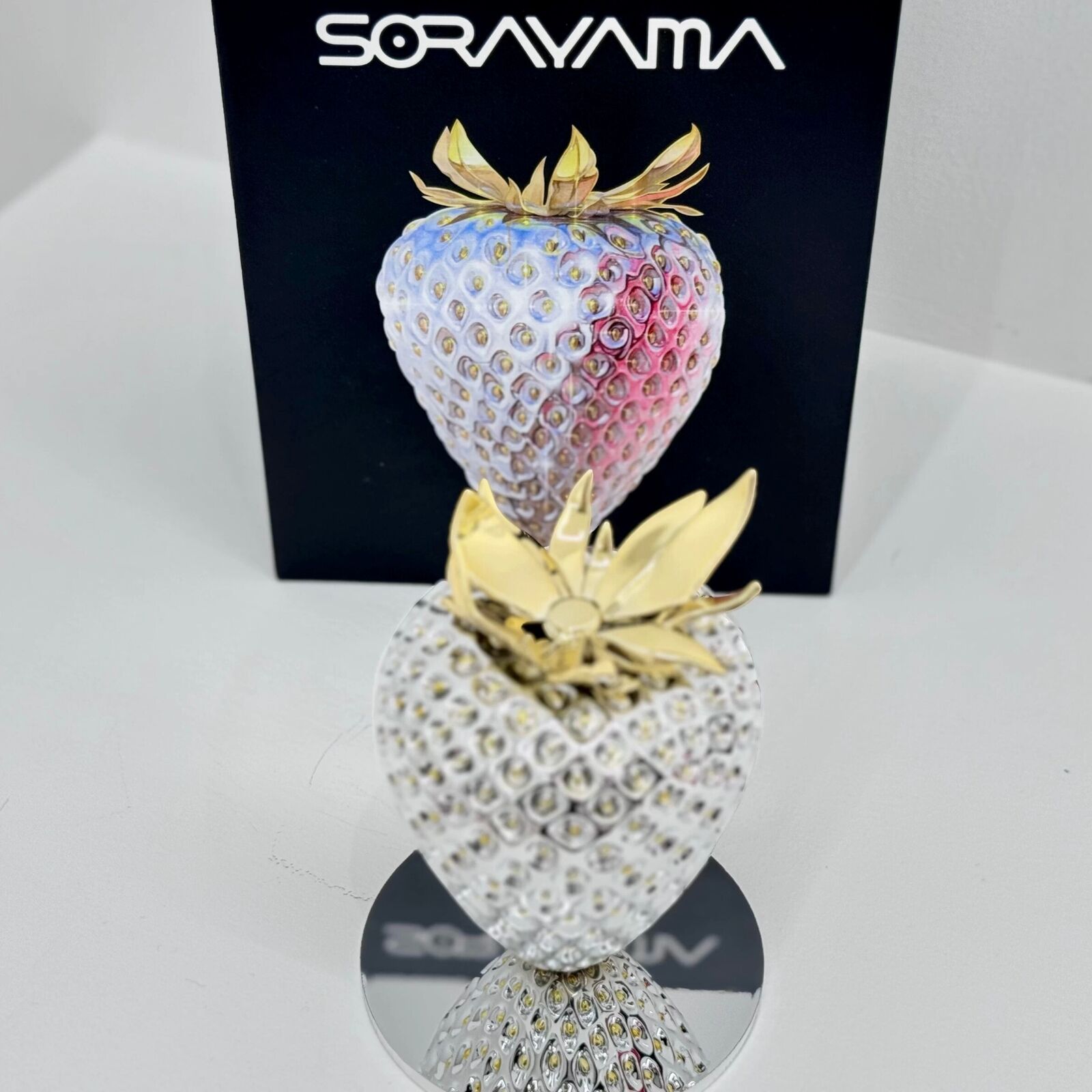 A silver and gold strawberry on a white background.