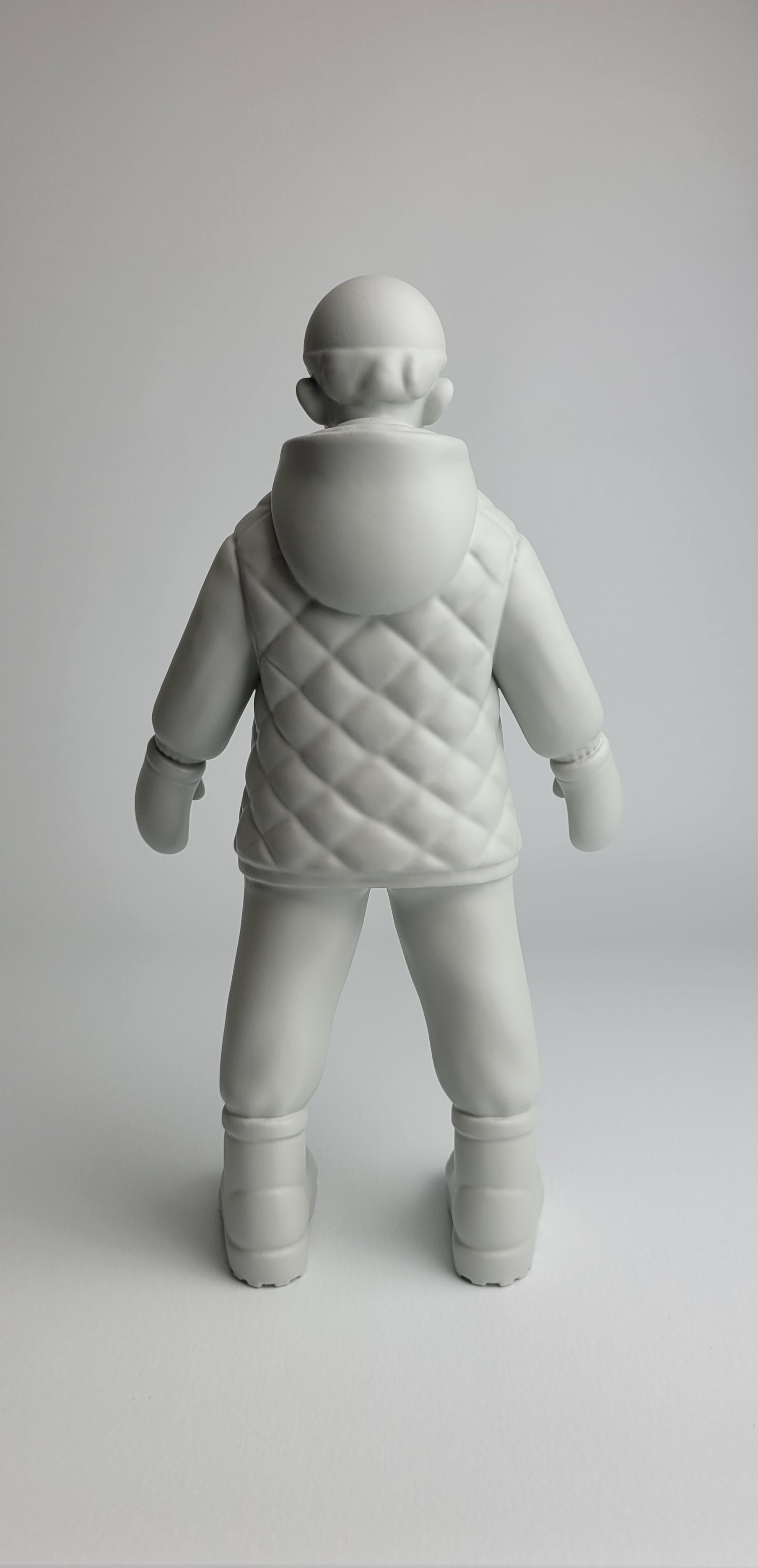 A monochromatic sculpture of a figure in winter gear standing against a neutral background.