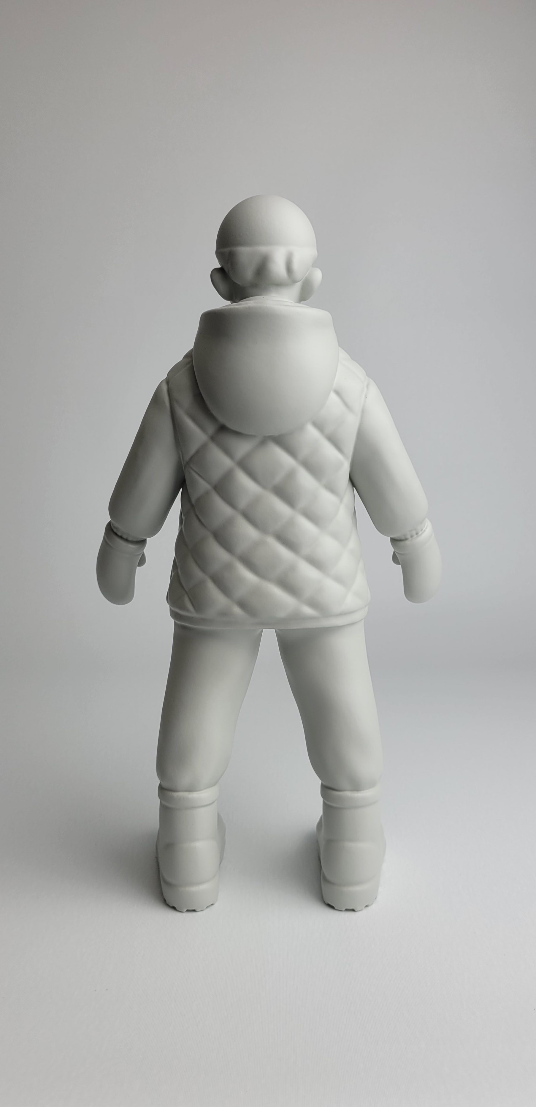 A monochromatic sculpture of a figure in winter gear standing against a neutral background.