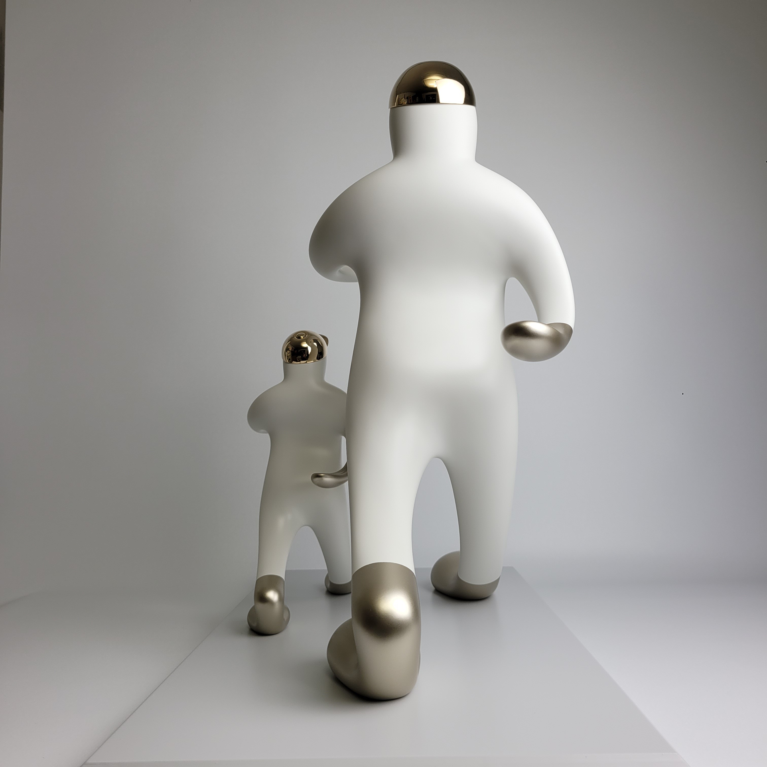 A playful sculpture of two figures in a matching pose, featuring smooth white forms with metallic accents.