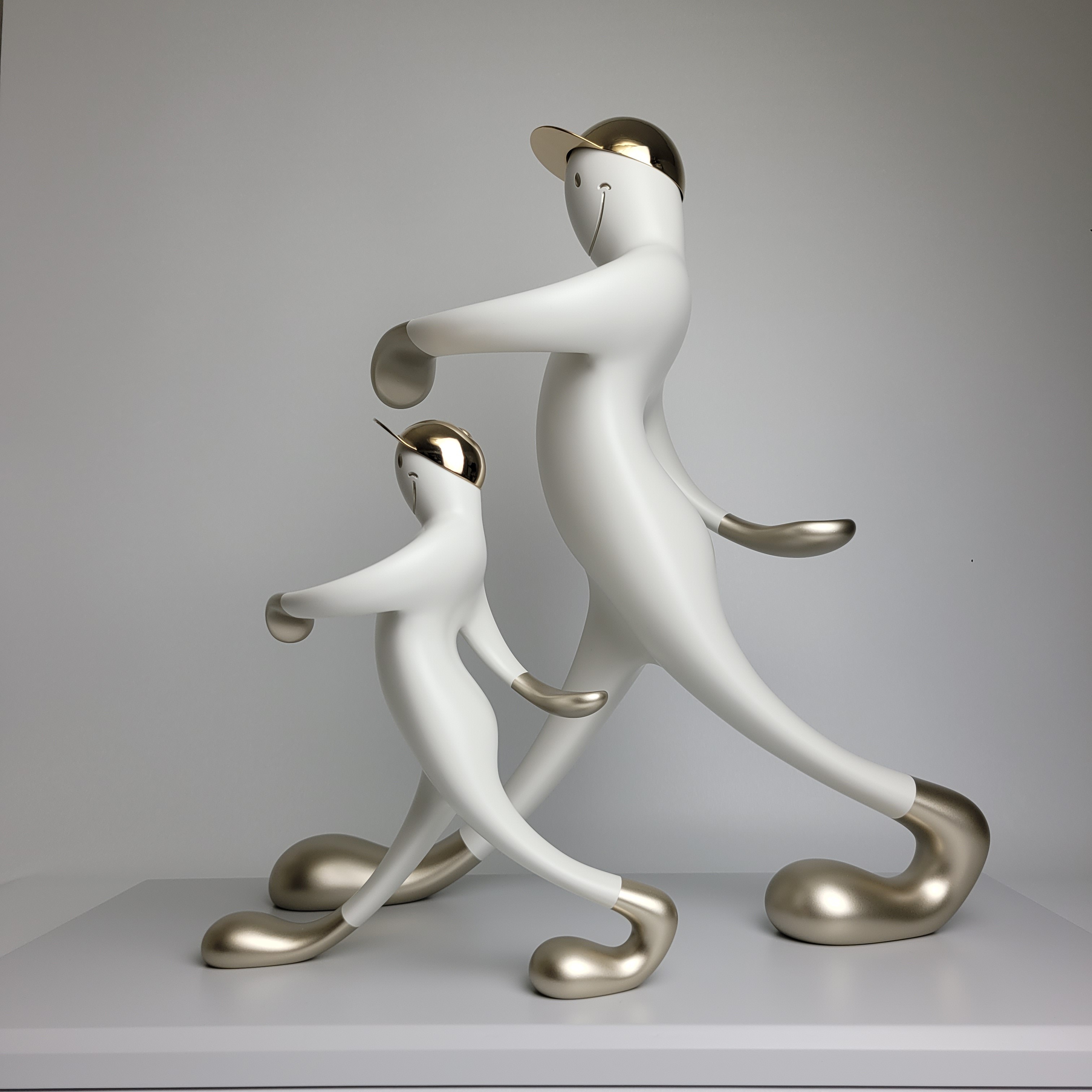 A playful sculpture of two figures in a matching pose, featuring smooth white forms with metallic accents.