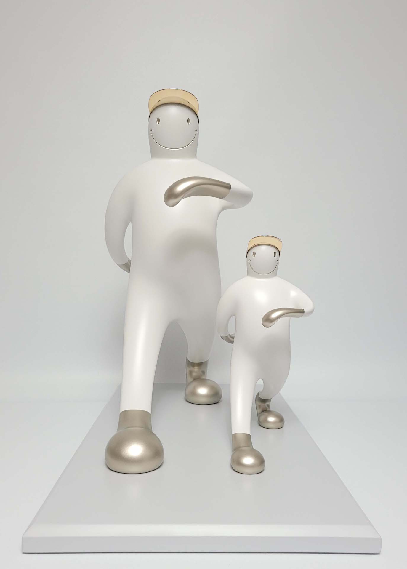 A playful sculpture of two figures in a matching pose, featuring smooth white forms with metallic accents.