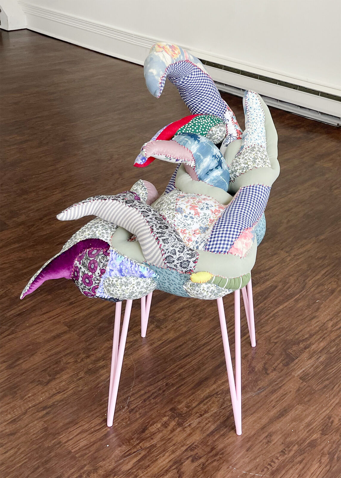 A whimsical chair with a patchwork quilt seat and slender pink legs.