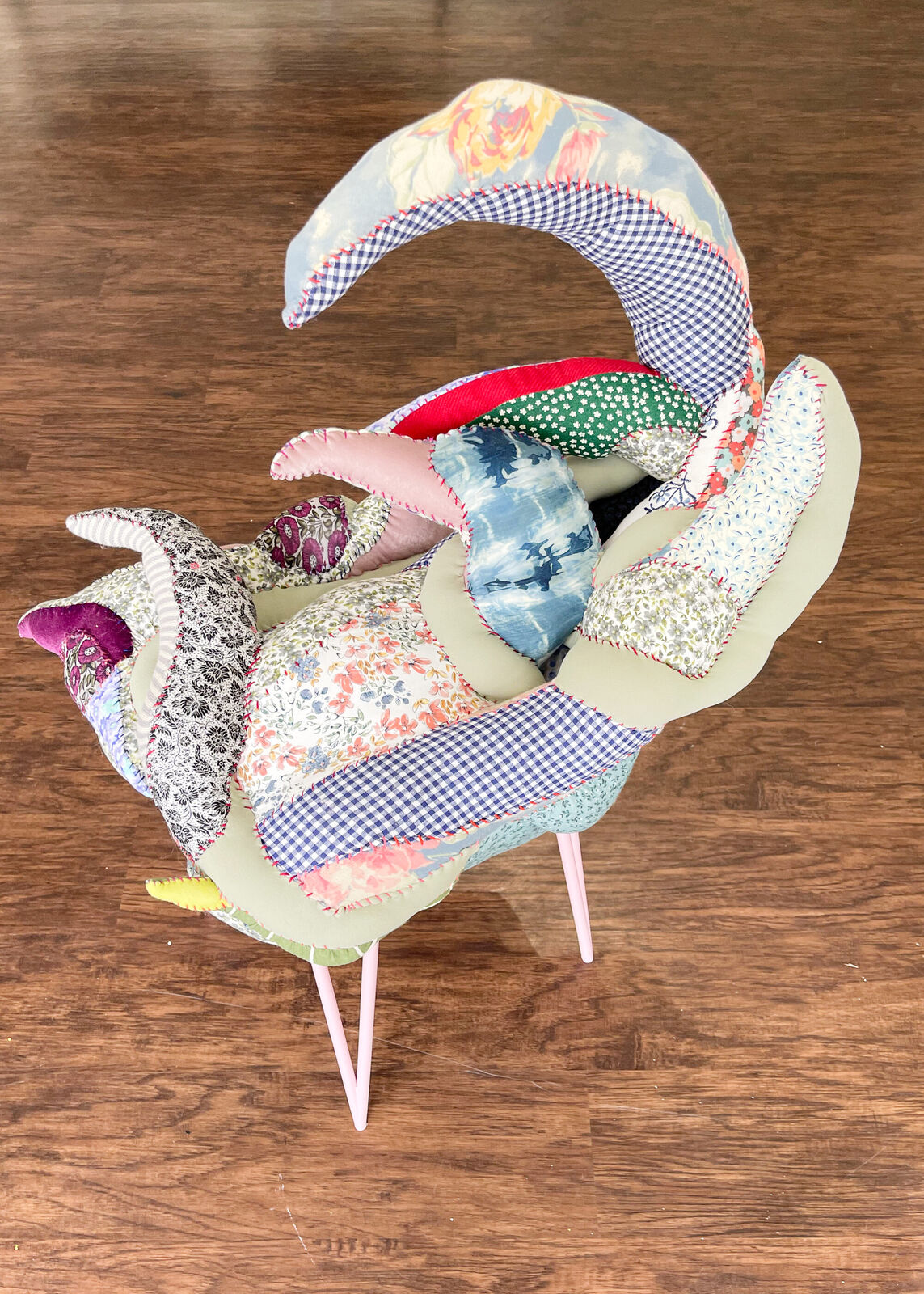 A whimsical chair with a patchwork quilt seat and slender pink legs.