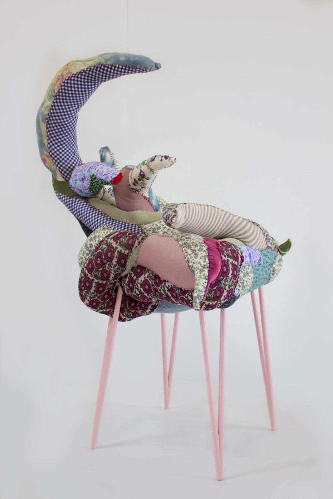 A whimsical chair with a patchwork quilt seat and slender pink legs.