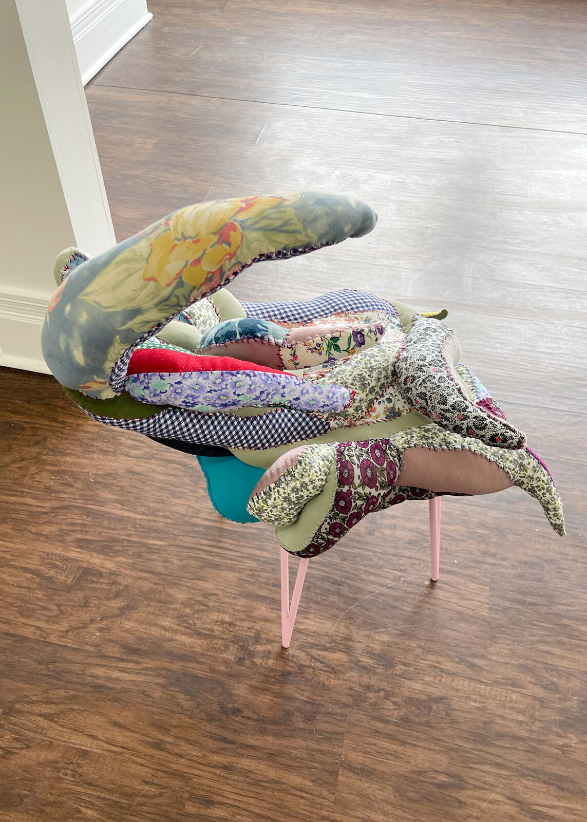 A whimsical chair with a patchwork quilt seat and slender pink legs.