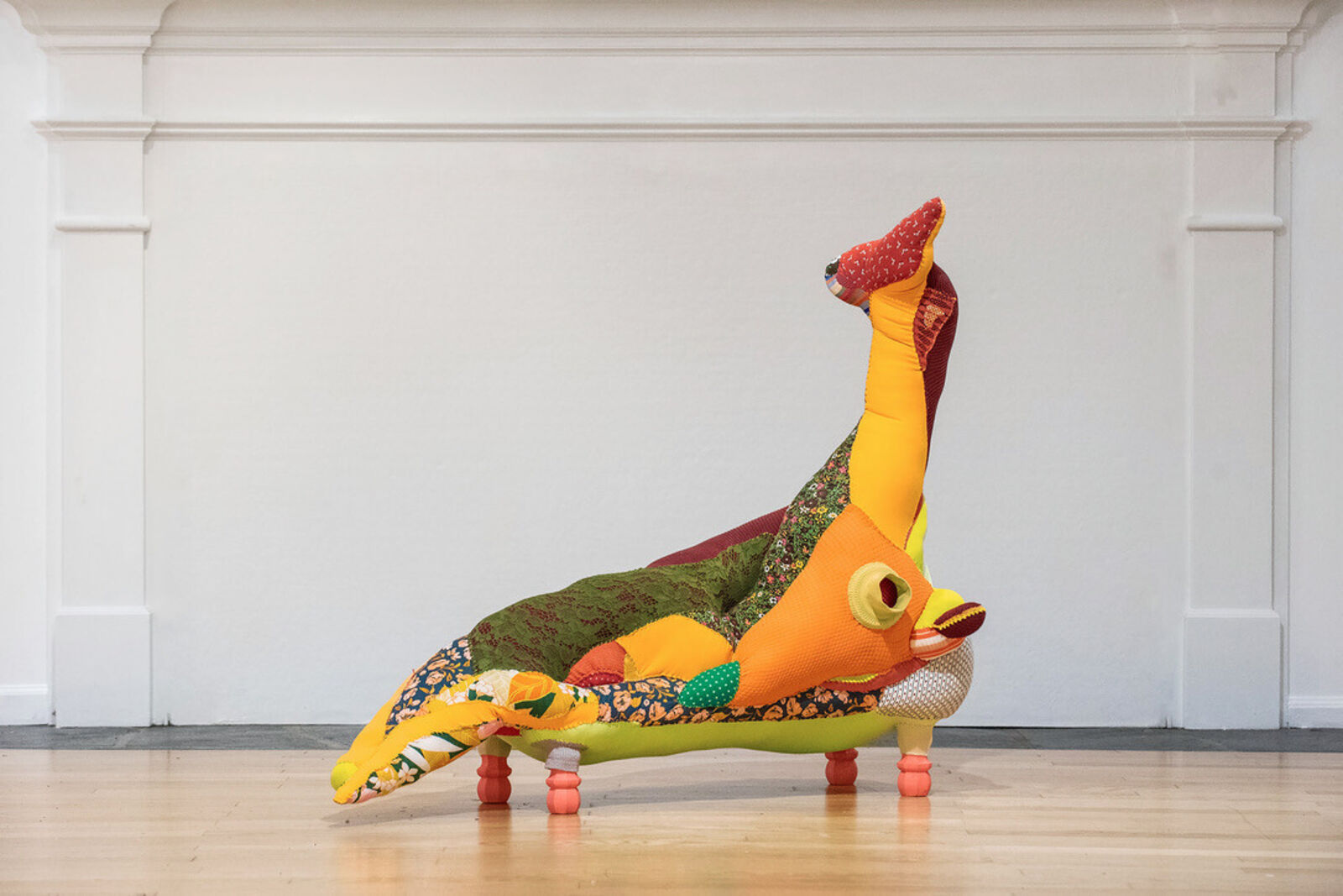 A colorful, patchwork-style lounge chair shaped like a reclining figure with an upward-extended leg.