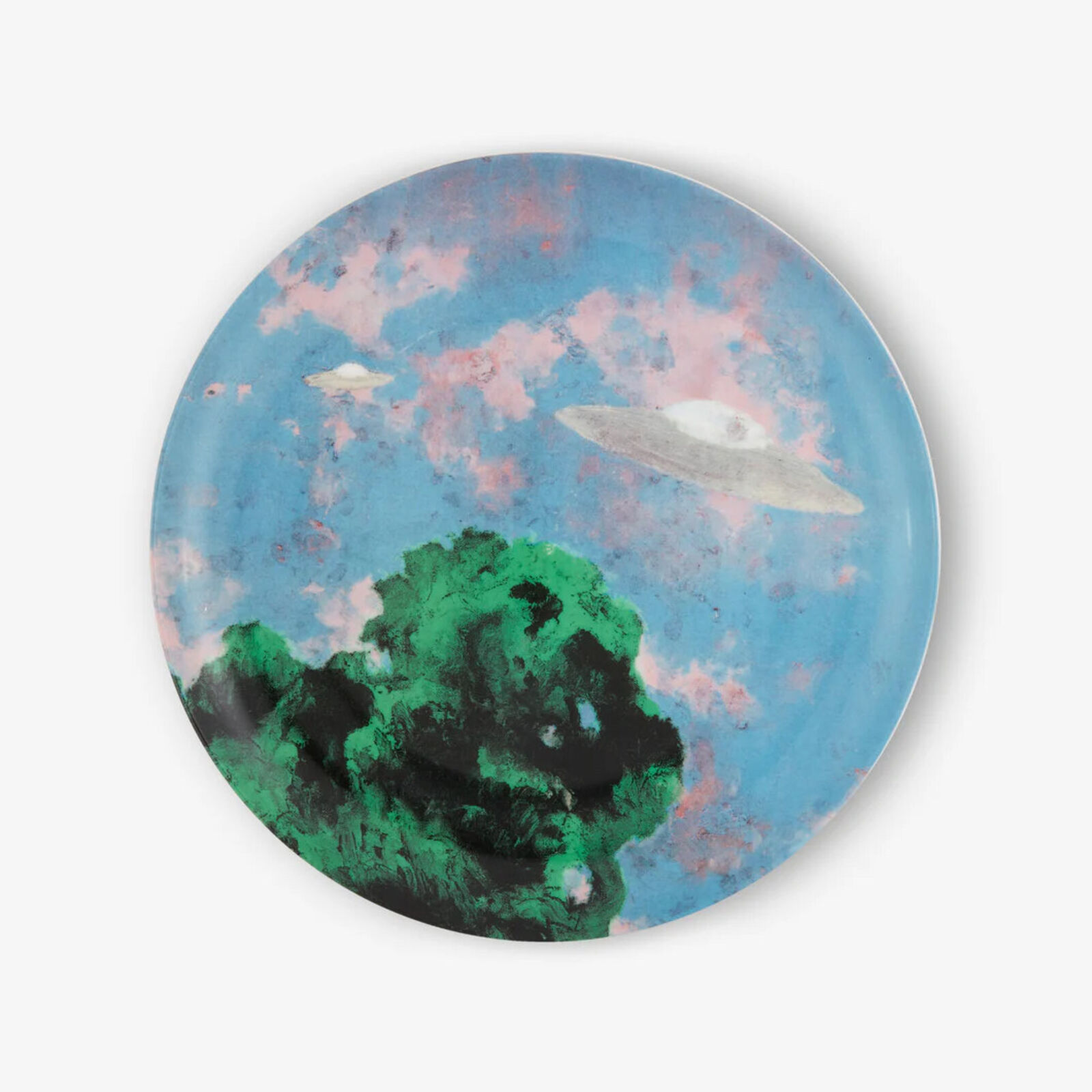 A plate with a painting of a UFO flying over a tree.