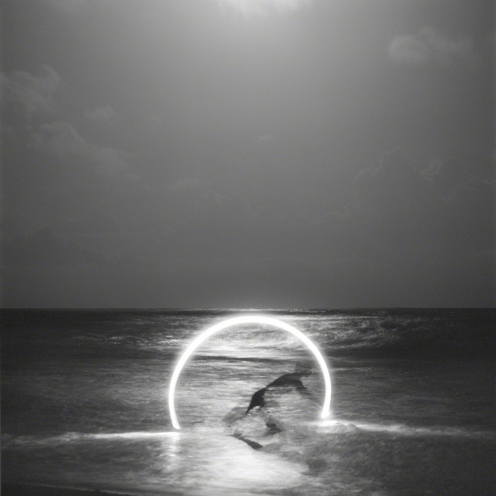 A surreal black-and-white seascape featuring a glowing ring of light over the ocean.