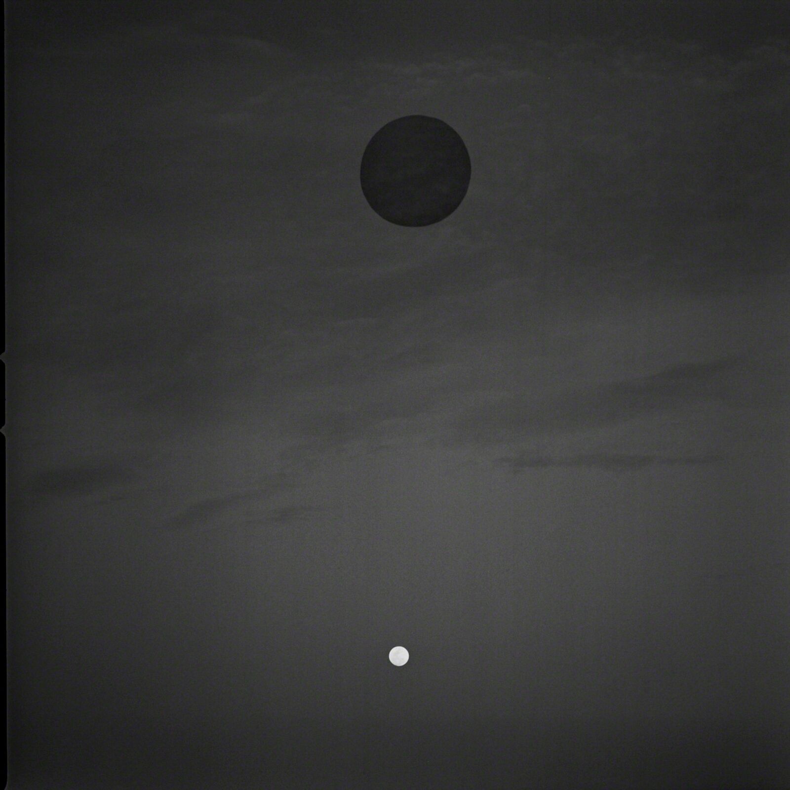 A minimalist black and white composition featuring a large dark circle and a small light dot against a cloudy sky.