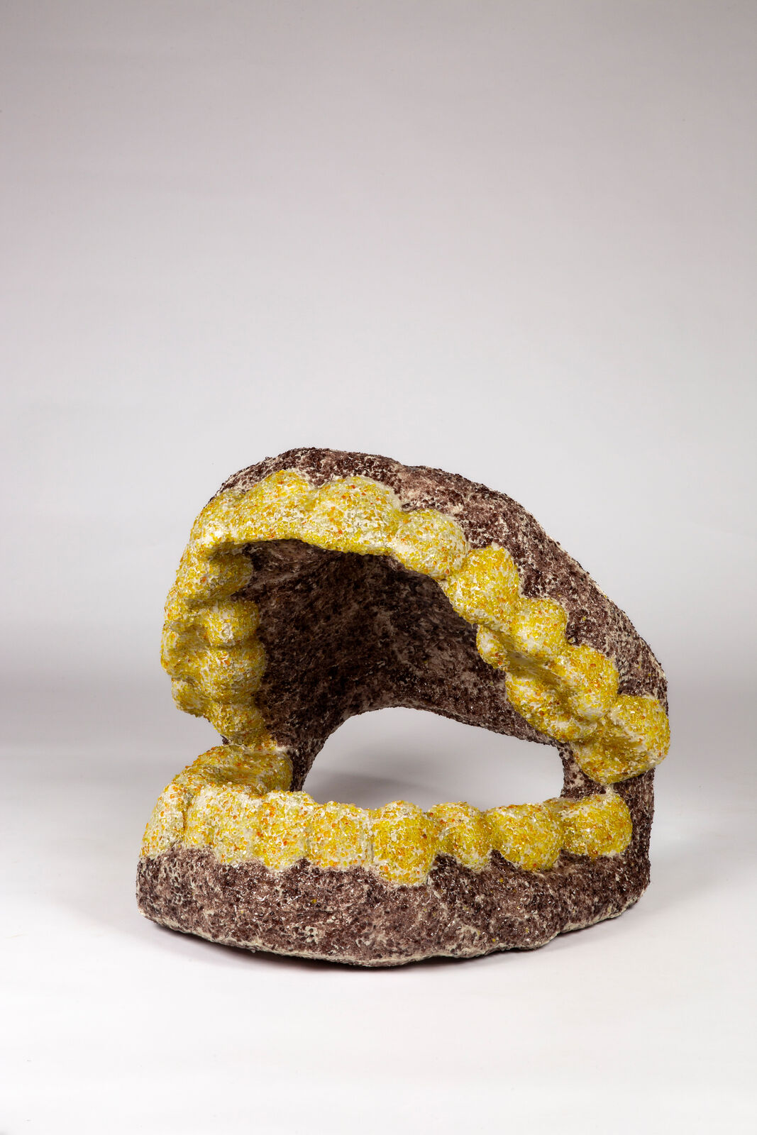 A sculptural piece resembling a mouth with yellow teeth against a plain background.
