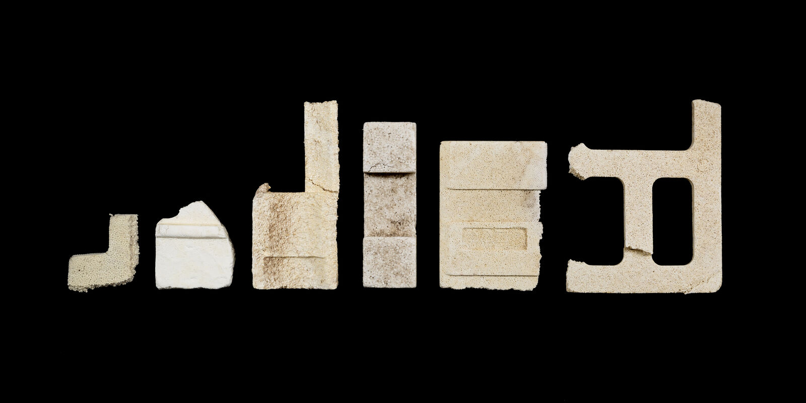 A row of seven textured, cream-colored blocks arranged in a horizontal line against a solid black background.
