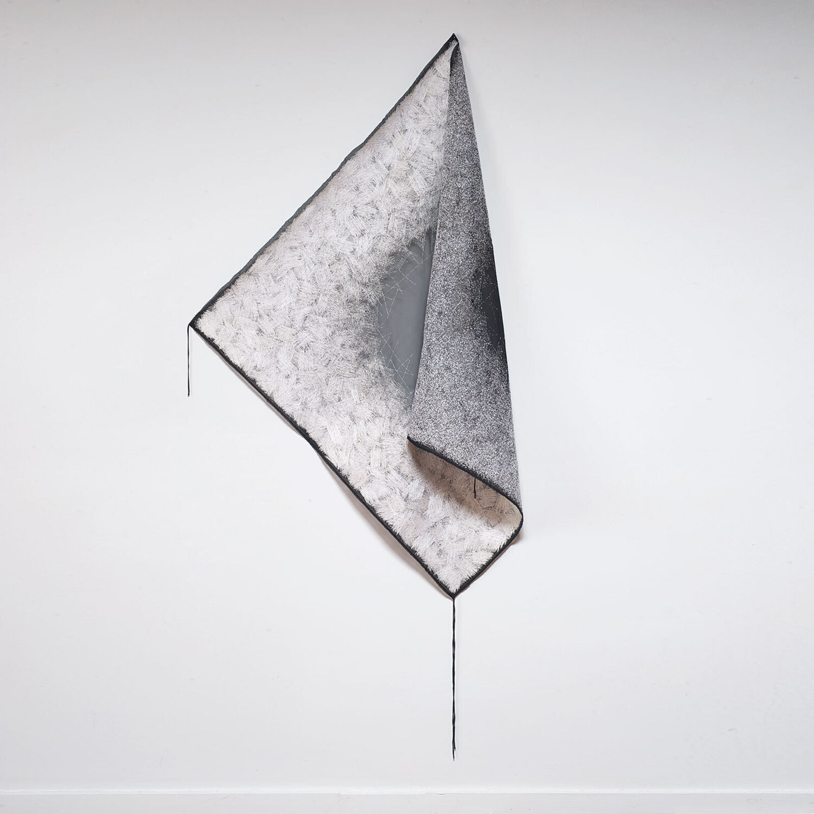 A minimalist textile sculpture featuring a folded triangular form with contrasting textures.