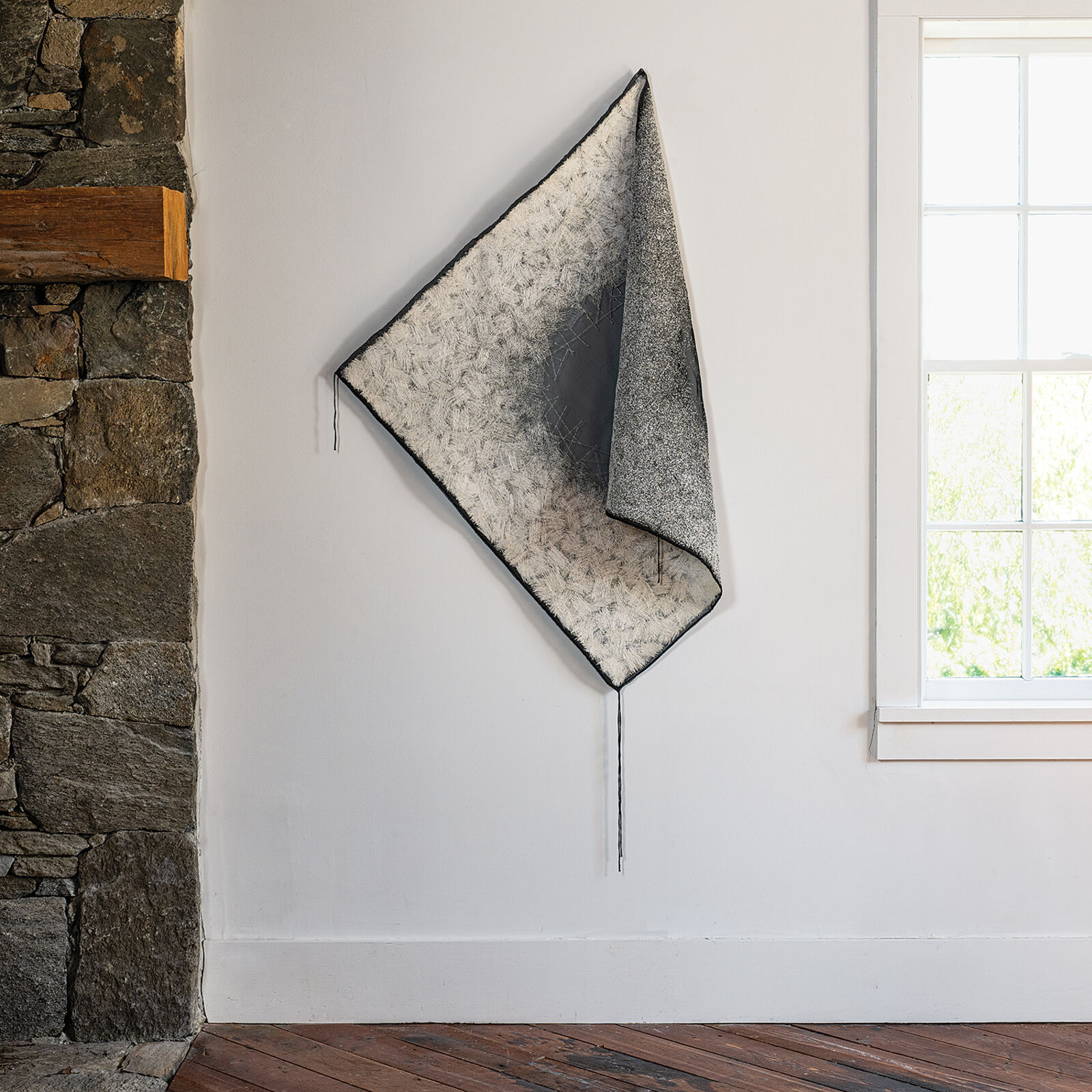 A minimalist textile sculpture featuring a folded triangular form with contrasting textures.