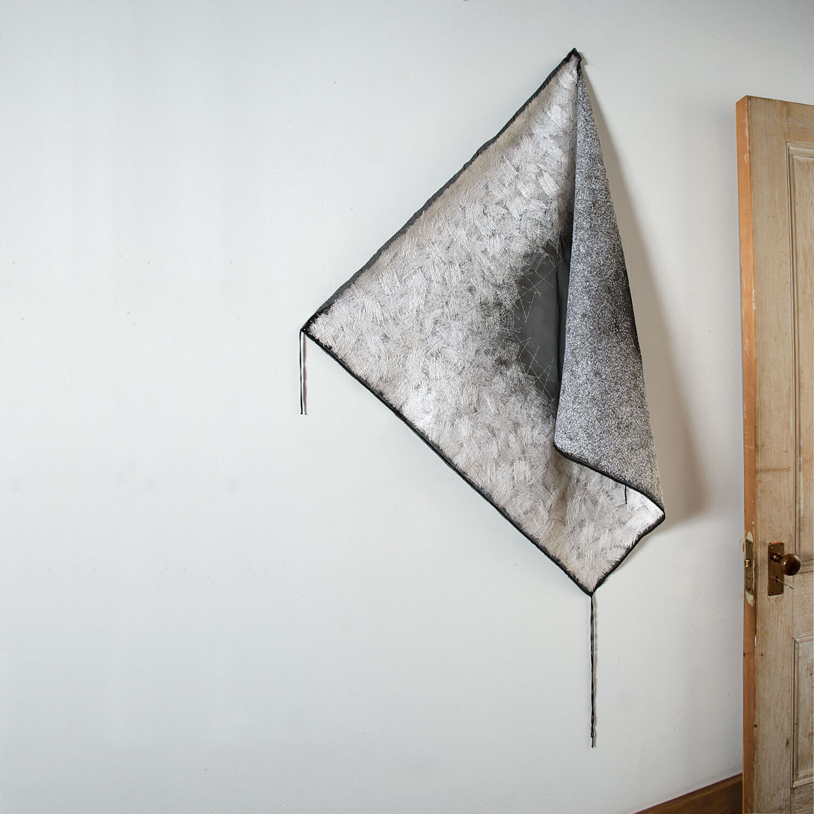 A minimalist textile sculpture featuring a folded triangular form with contrasting textures.