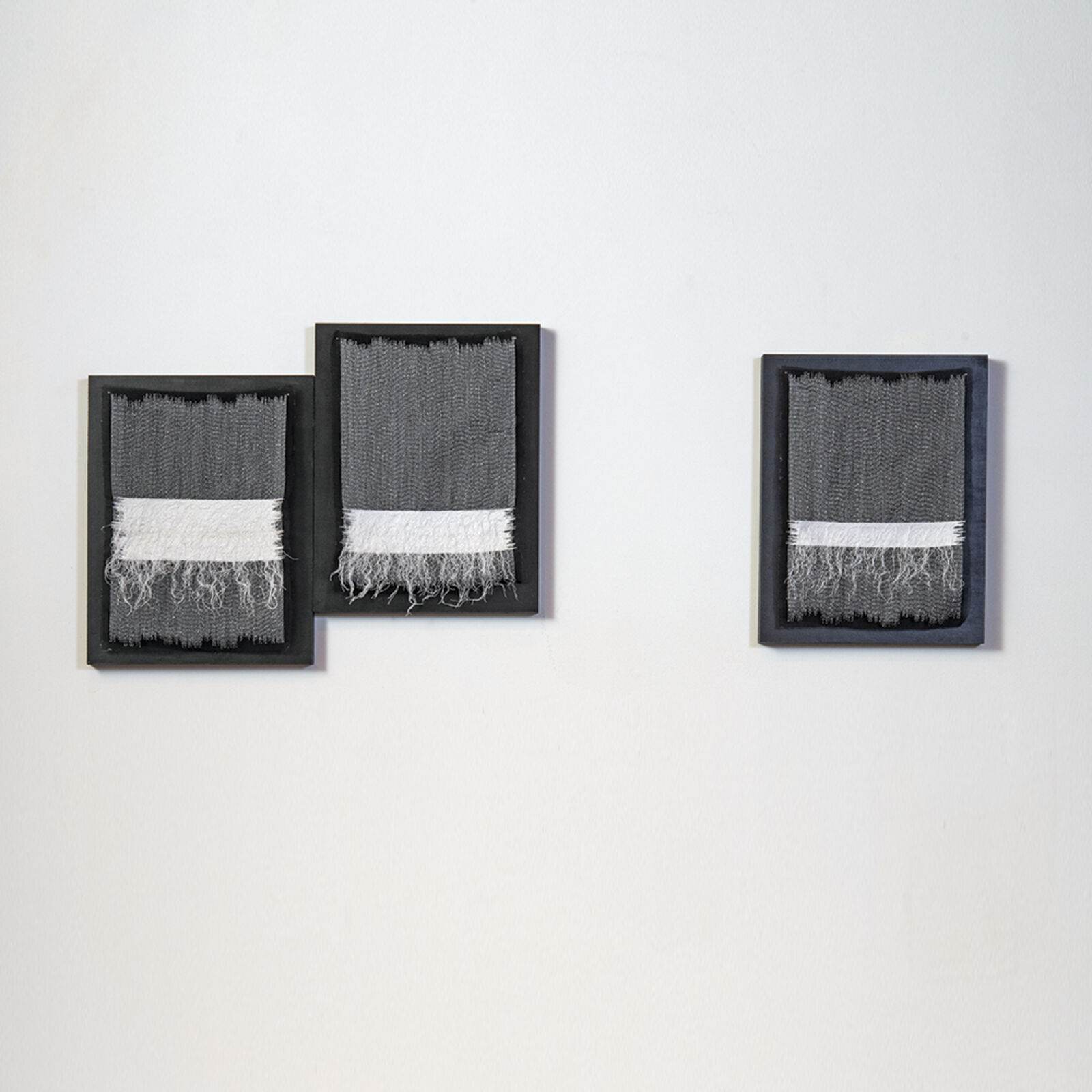 A minimalist wall installation featuring three framed textile pieces with a monochromatic palette.