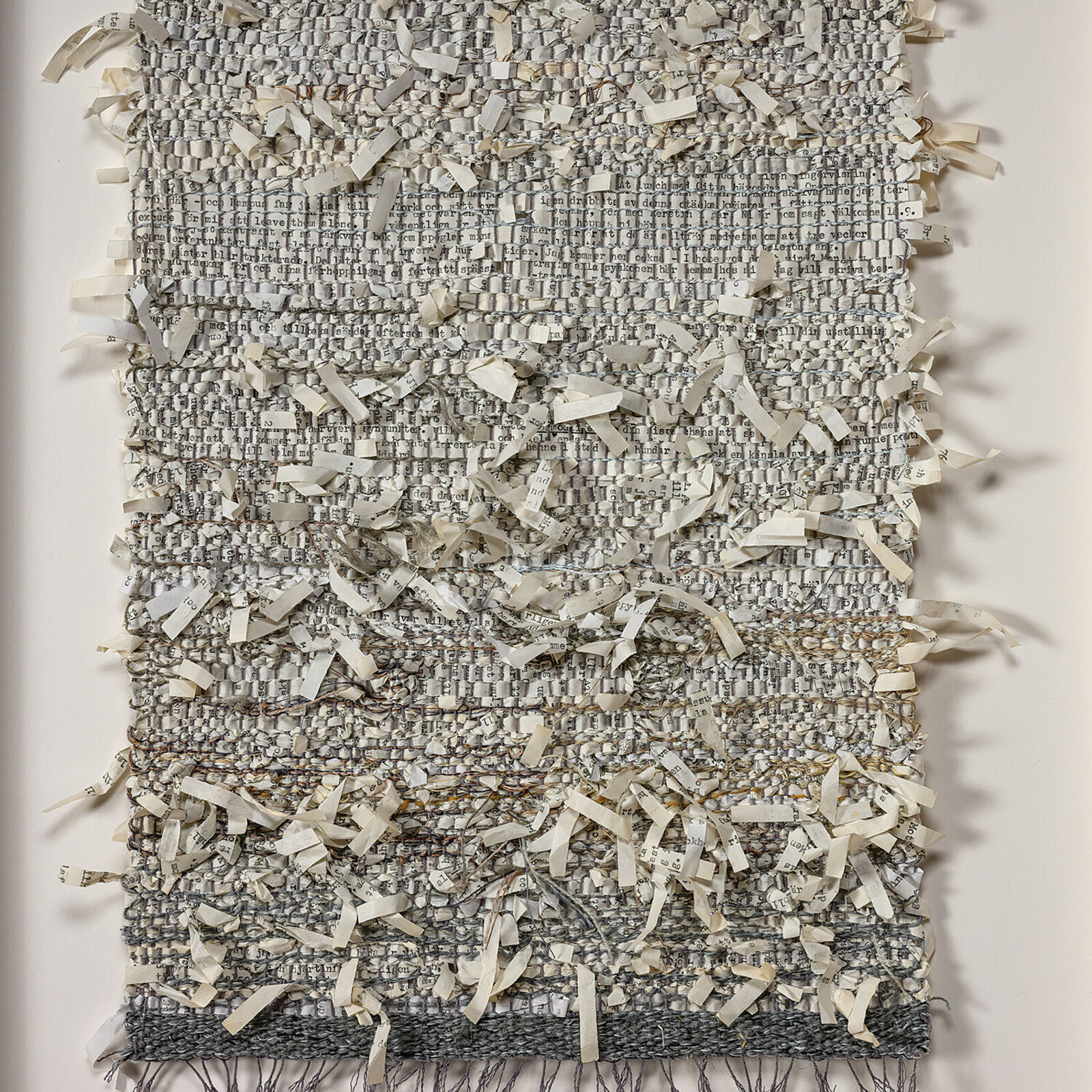 A framed textile artwork featuring a woven fabric with shredded paper strips layered on top.
