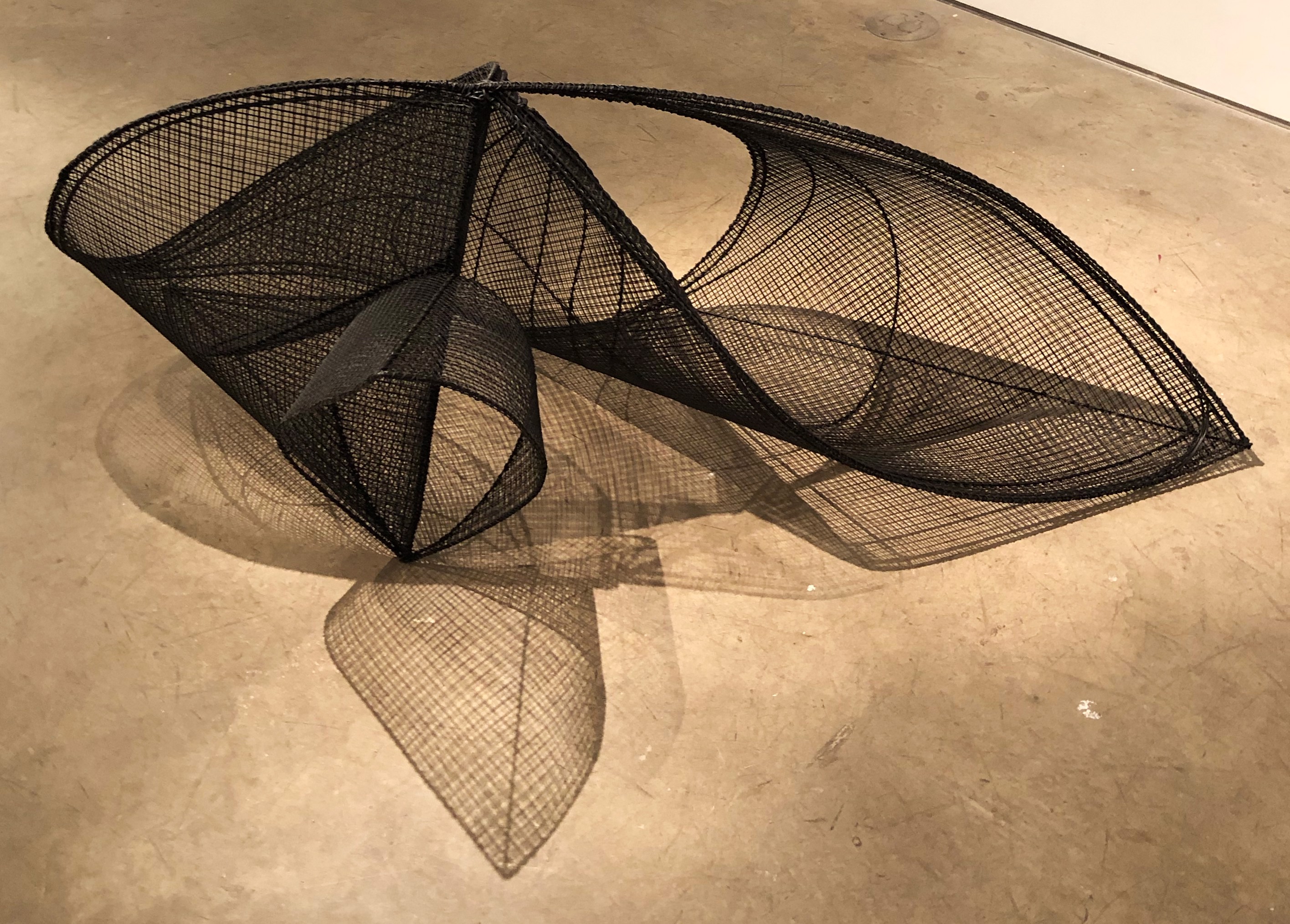 A black sculpture on a concrete surface with a shadow on the floor.