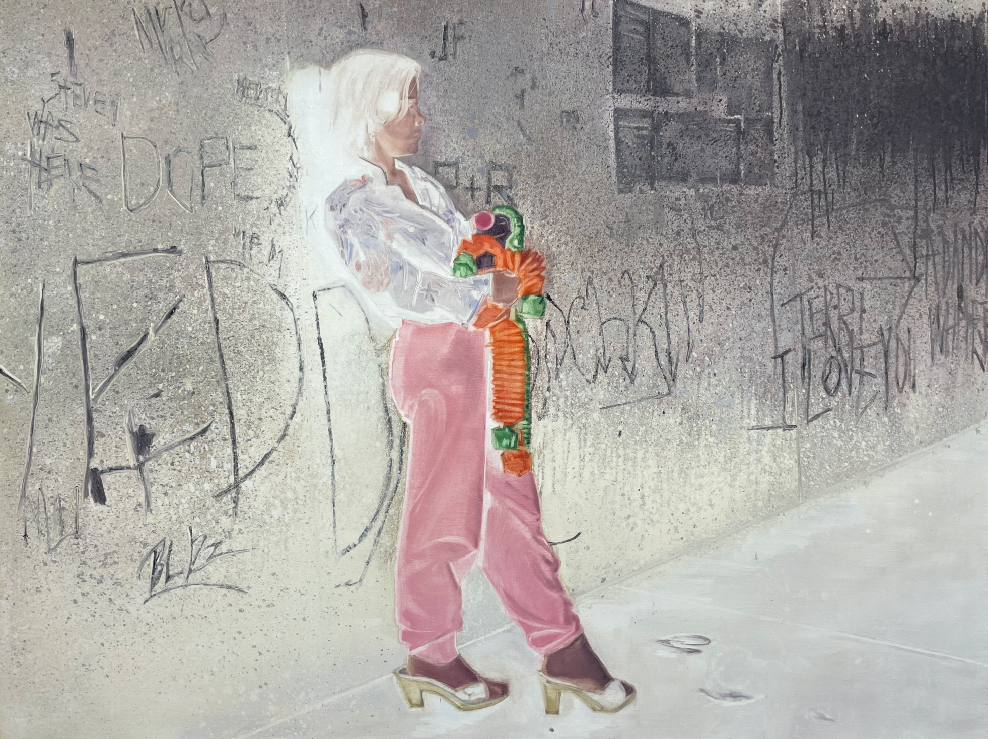 A figure in pink trousers and a white shirt leans against a graffiti-covered wall, clutching a colorful, abstract object.