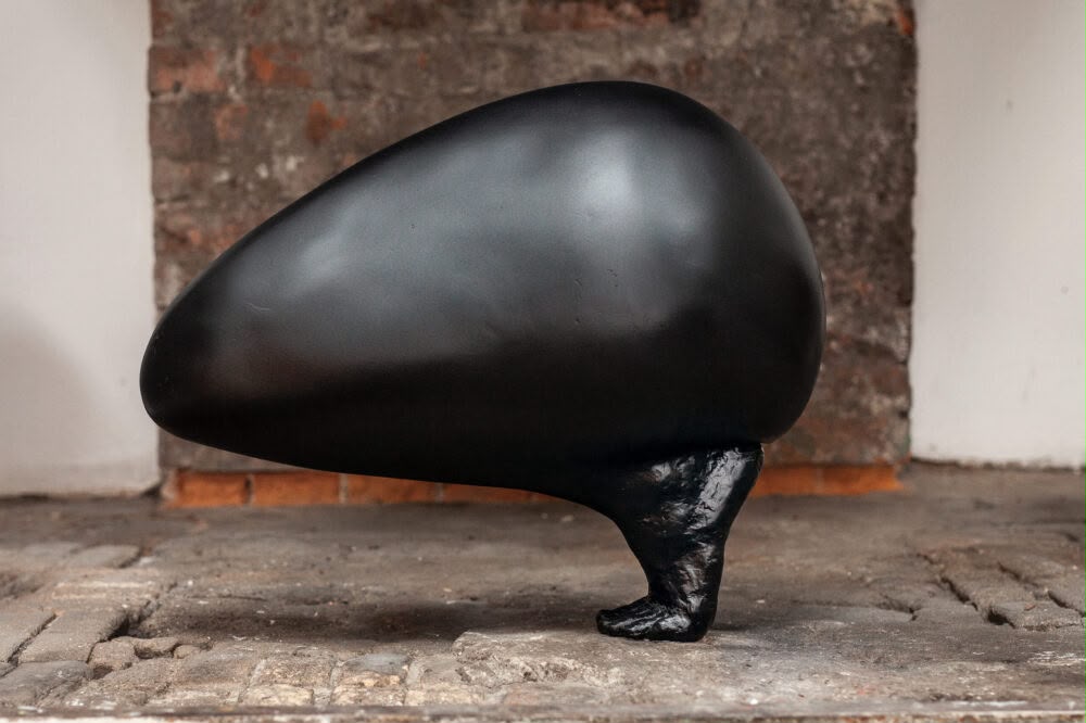 A black, egg-shaped sculpture supported by a single foot-like base.