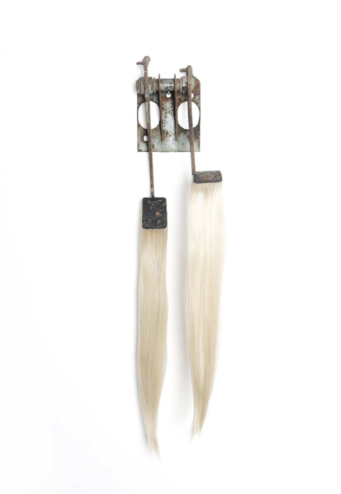 A vertical assemblage featuring a weathered metal bracket with two long, light-colored hair strands hanging from it.