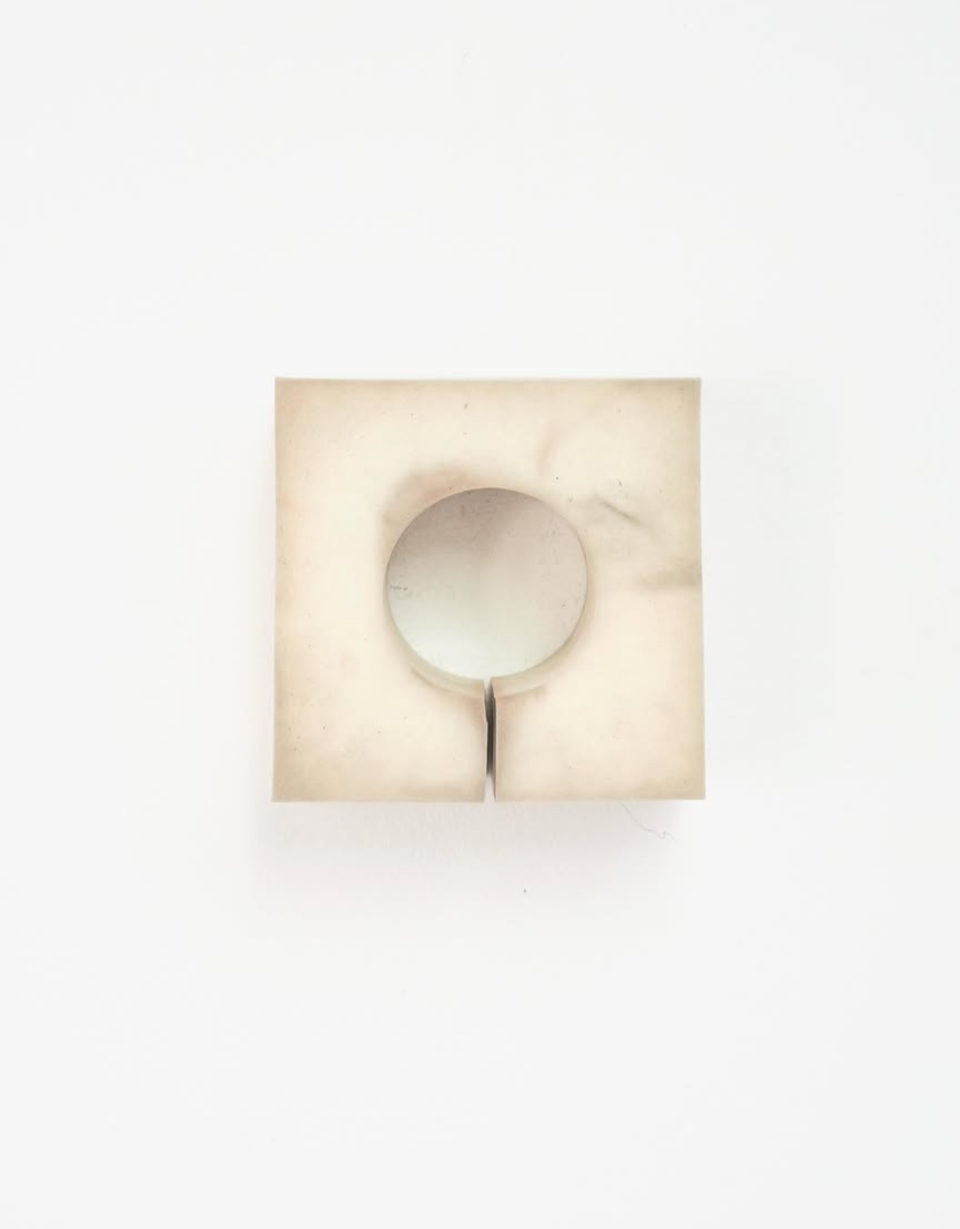 "A minimalist sculpture featuring a split square block with a circular cutout revealing a reflective surface."