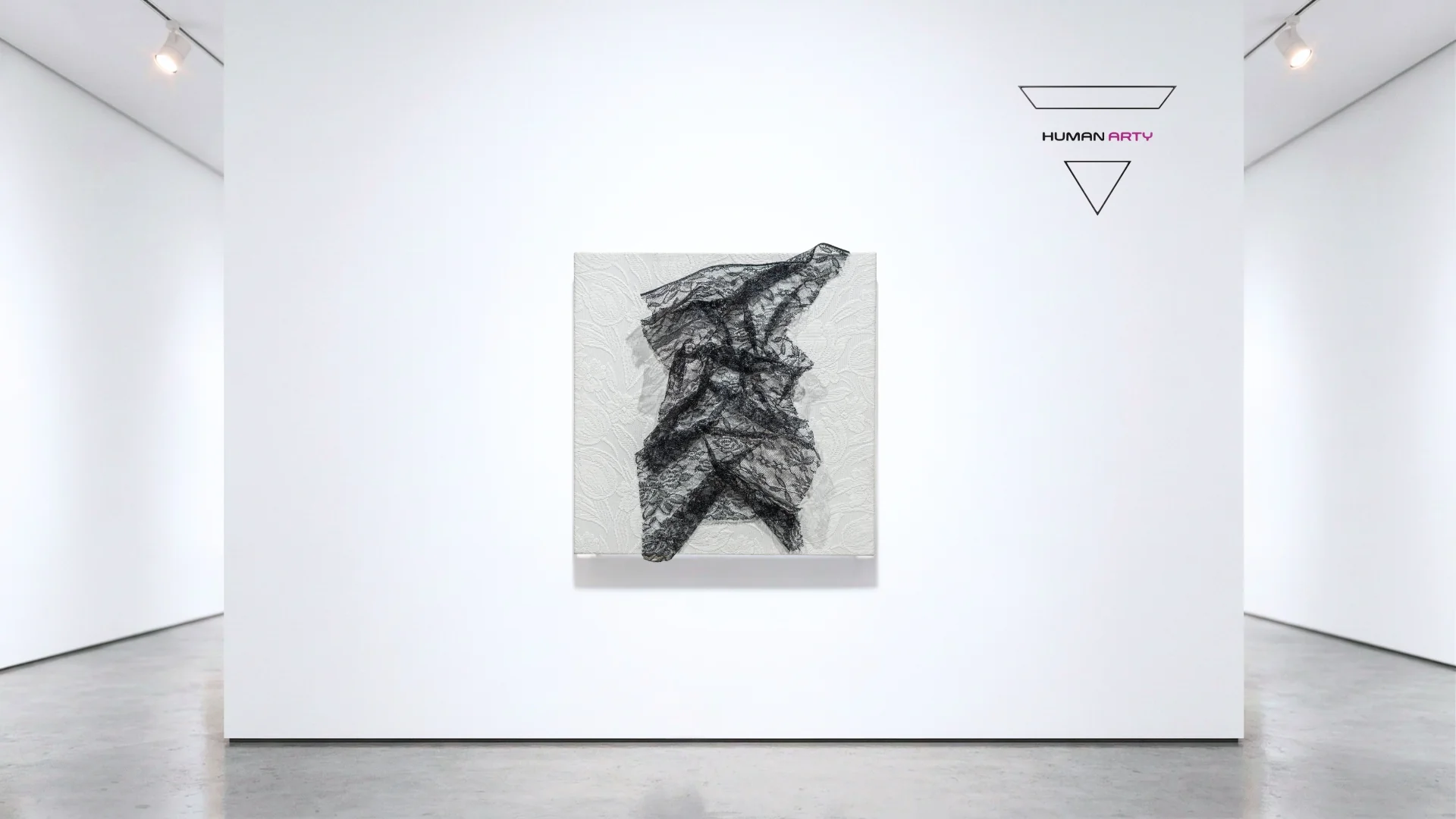 A minimalist gallery scene featuring a square canvas with black lace draped over it.