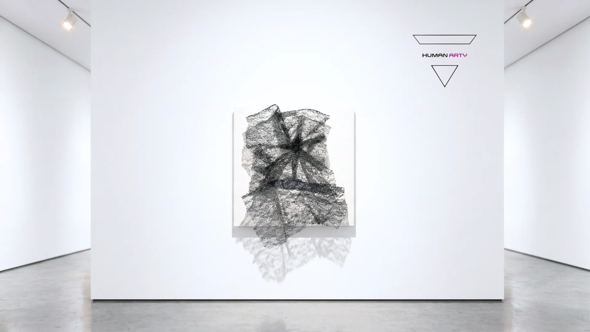A minimalist gallery space featuring a black lace-like sculpture mounted on a white wall.