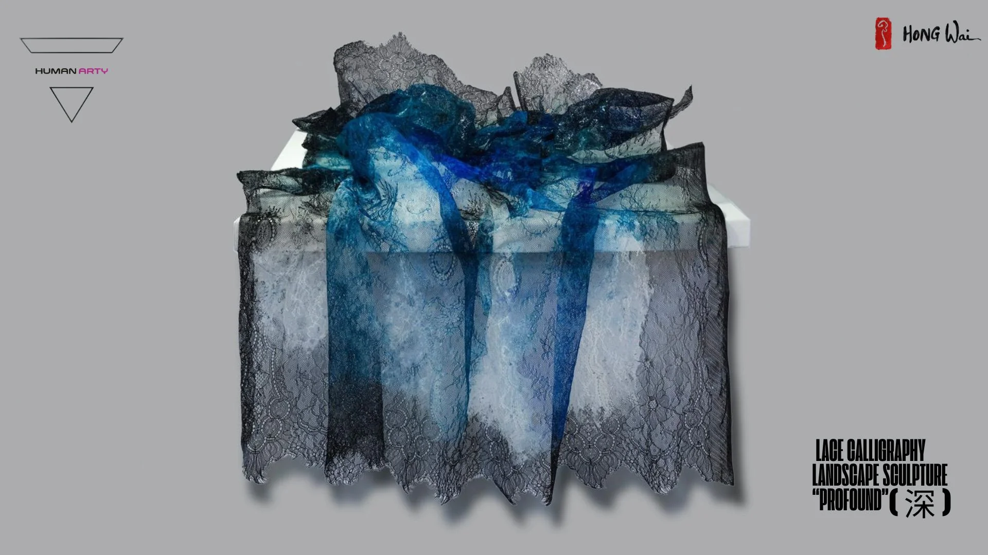 A sculptural arrangement of layered lace fabrics in deep blue and black tones, draped over a white rectangular base.