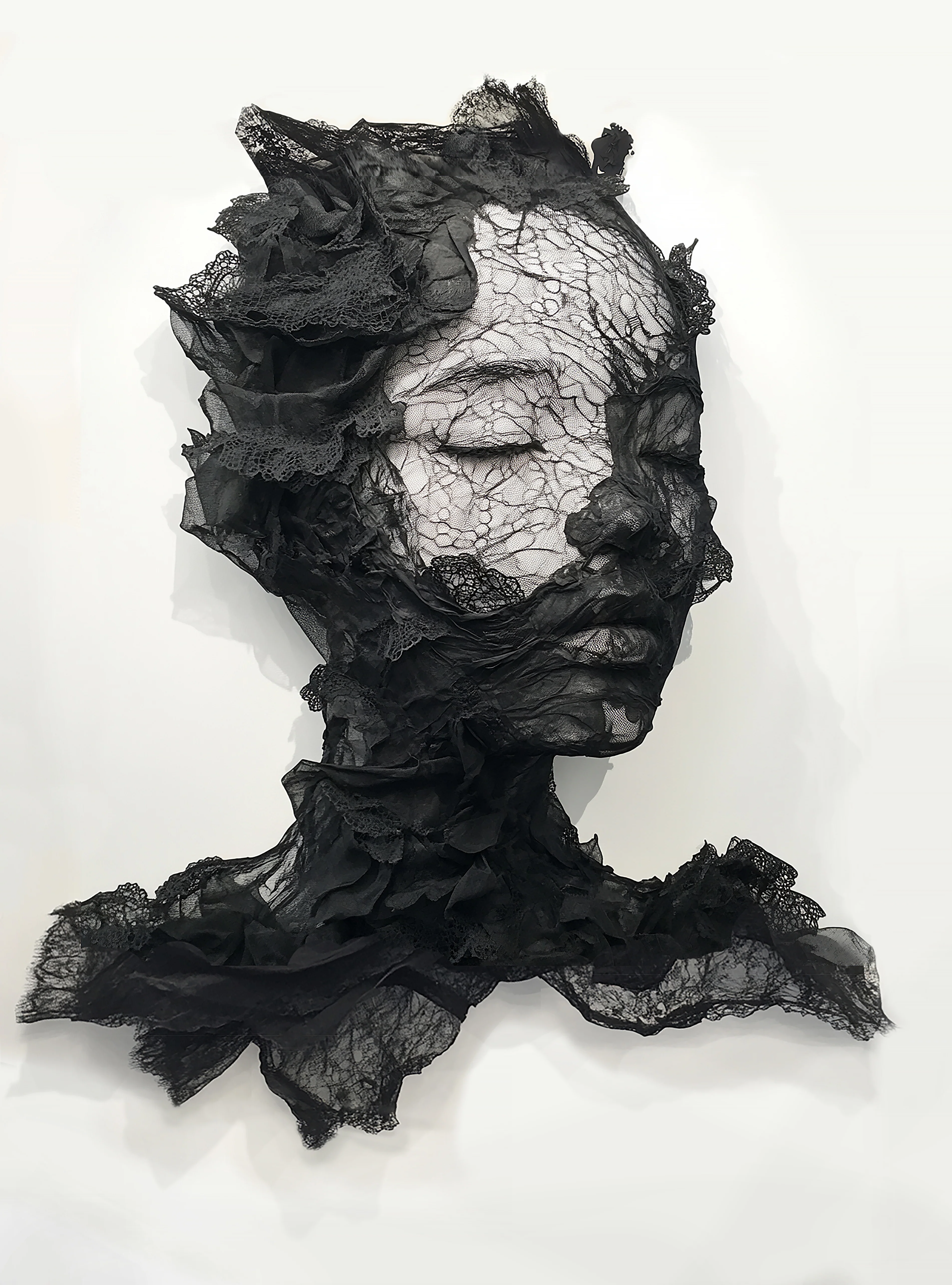 A monochromatic portrait of a sleeping figure constructed from textured black fabric against a stark white background.