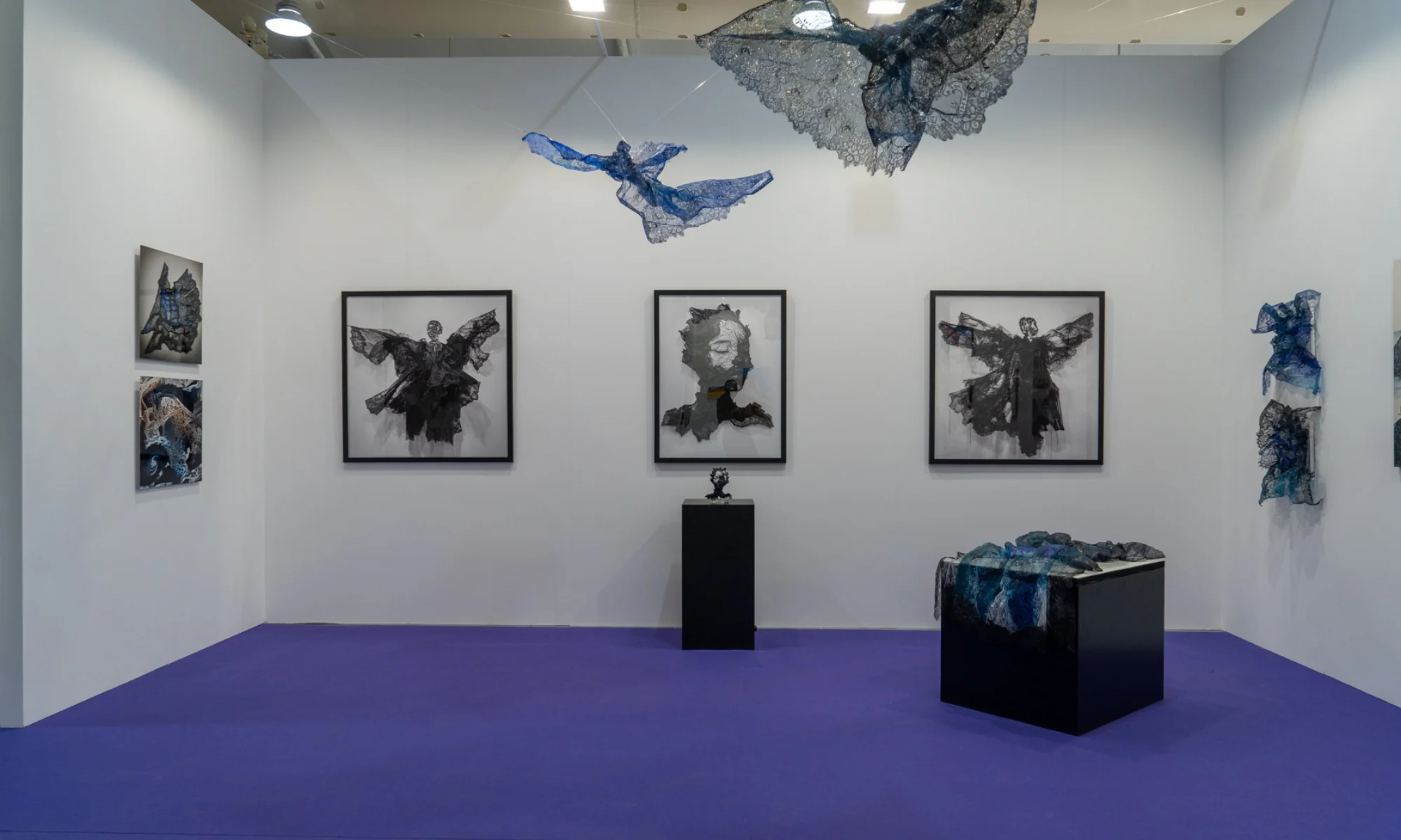 A framed black sculpture of a winged figure made from sheer, layered fabric against a stark white gallery wall.