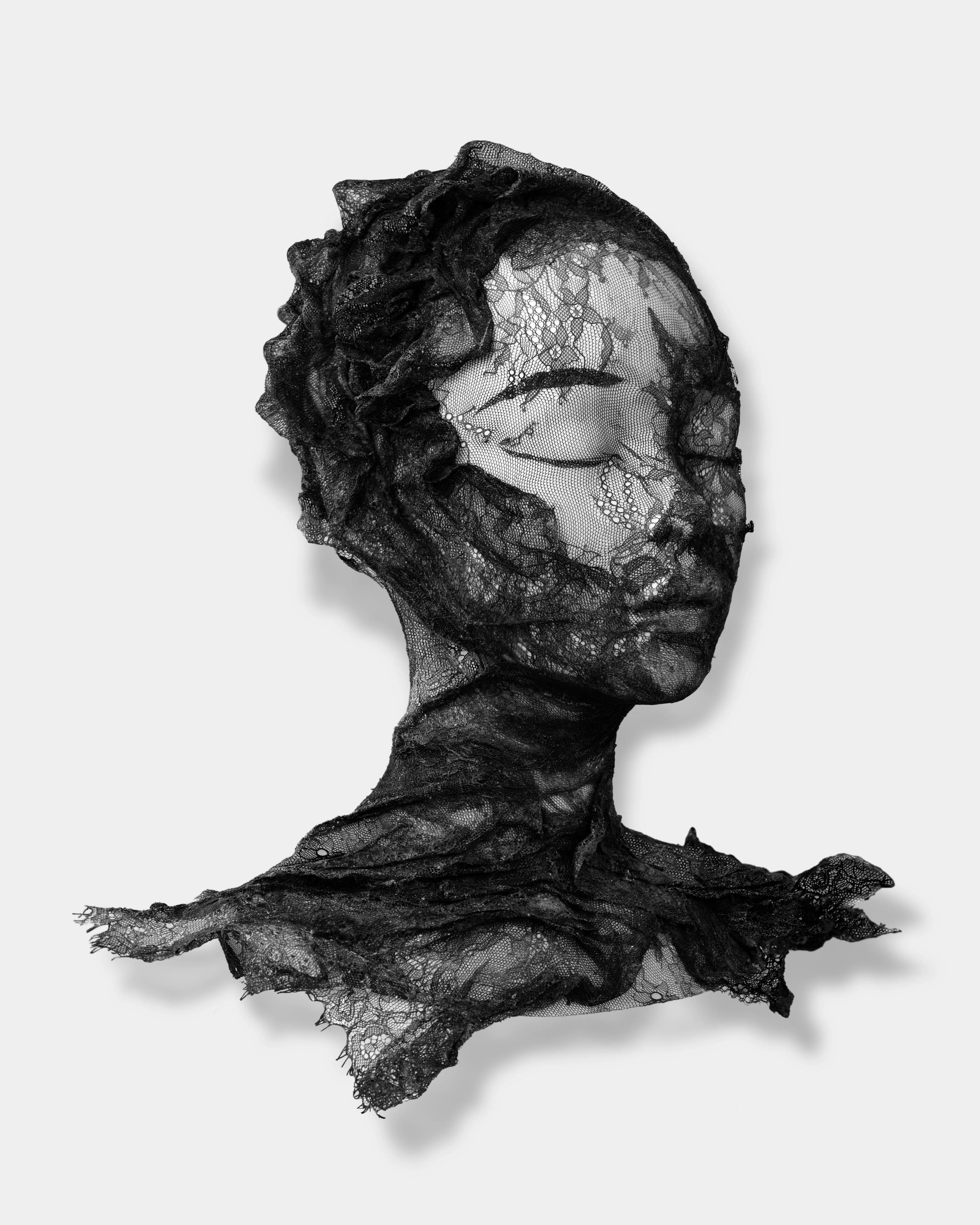 A bust sculpture of a face with closed eyes, crafted from intricate black lace and displayed on a purple pedestal.