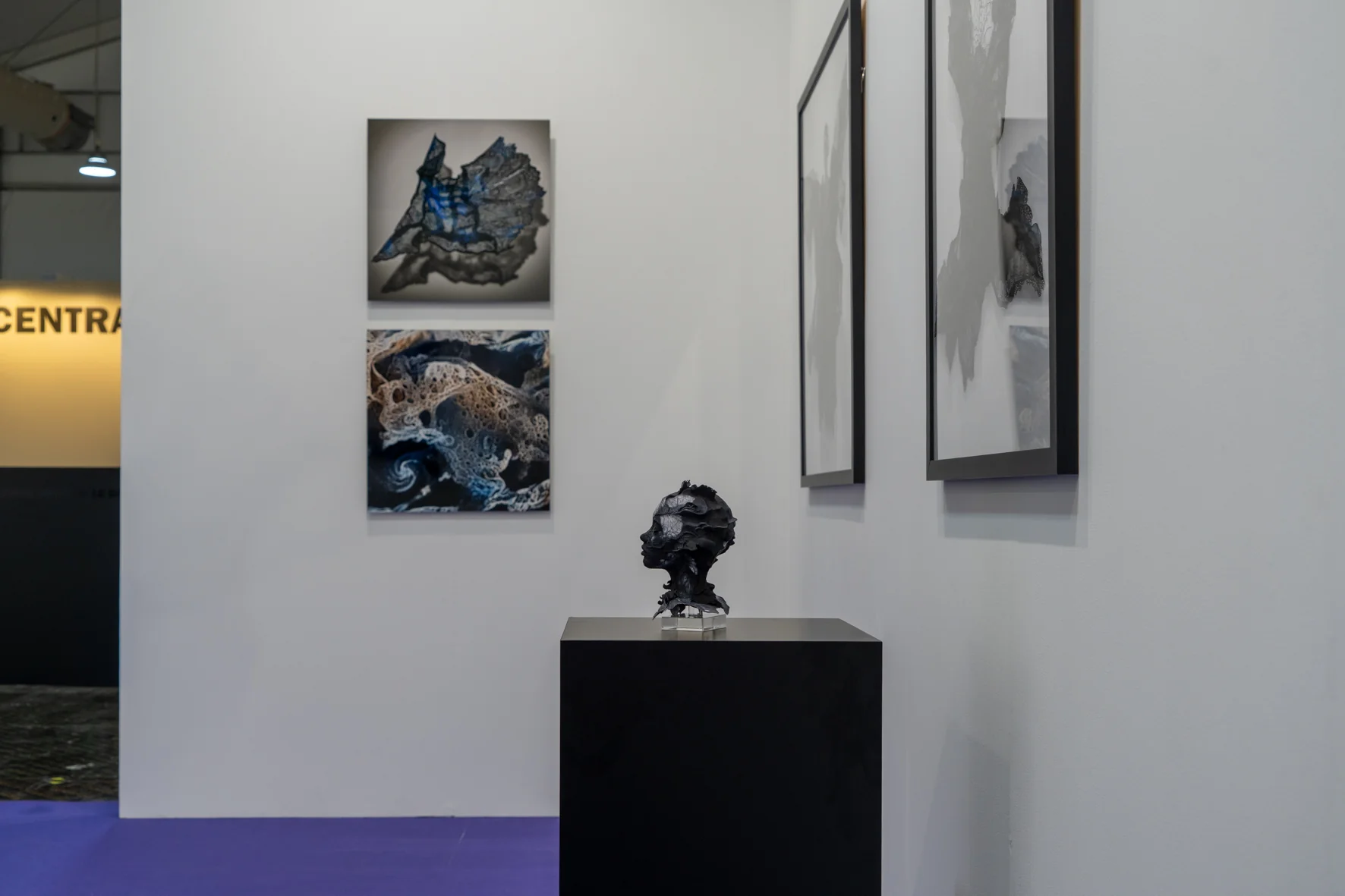 A surreal bust sculpture featuring a cracked, metallic face emerging from dark, organic textures.
