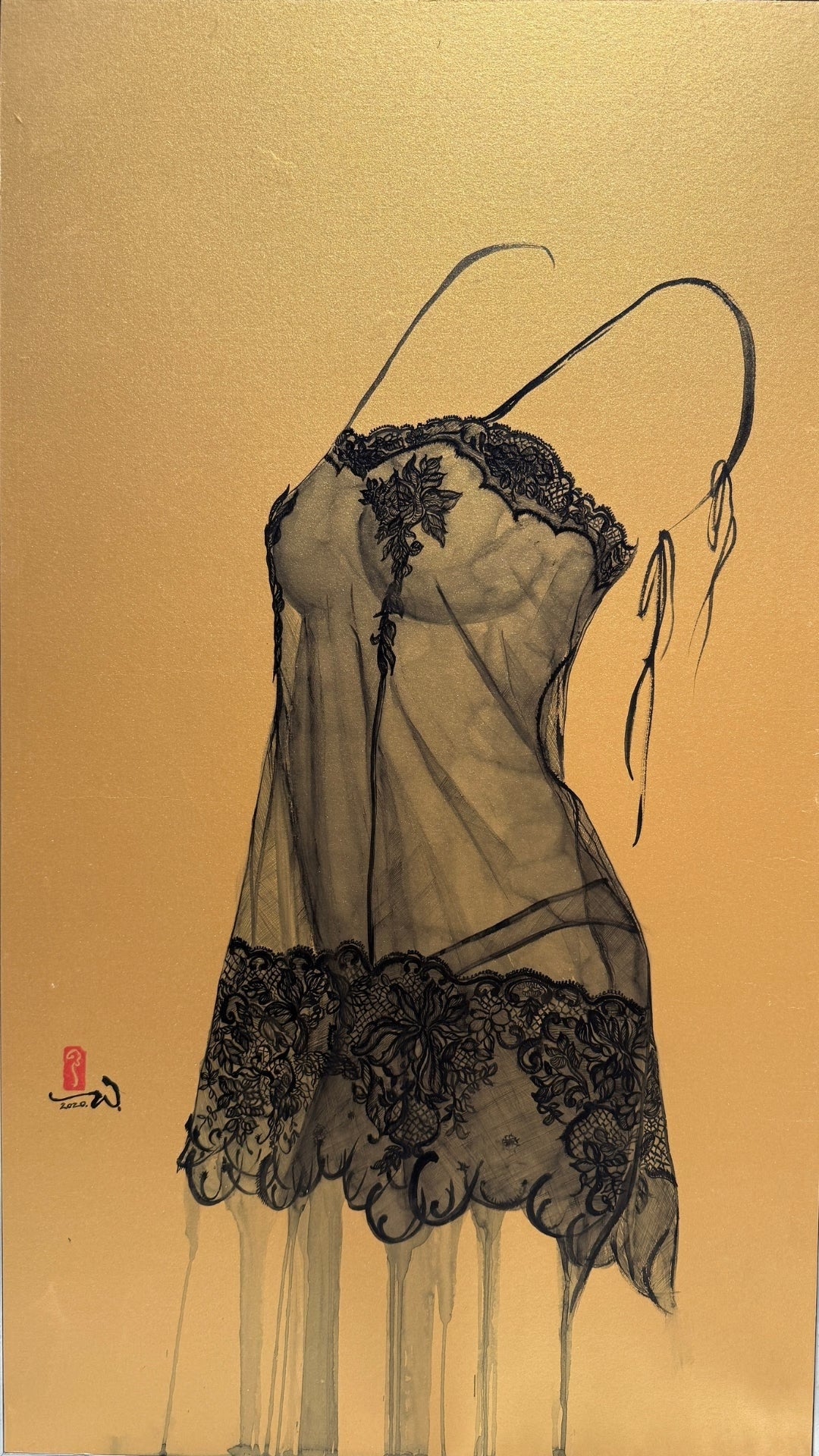 A framed artwork of a black lace garment against a textured gold background, displayed in a minimalist gallery space.