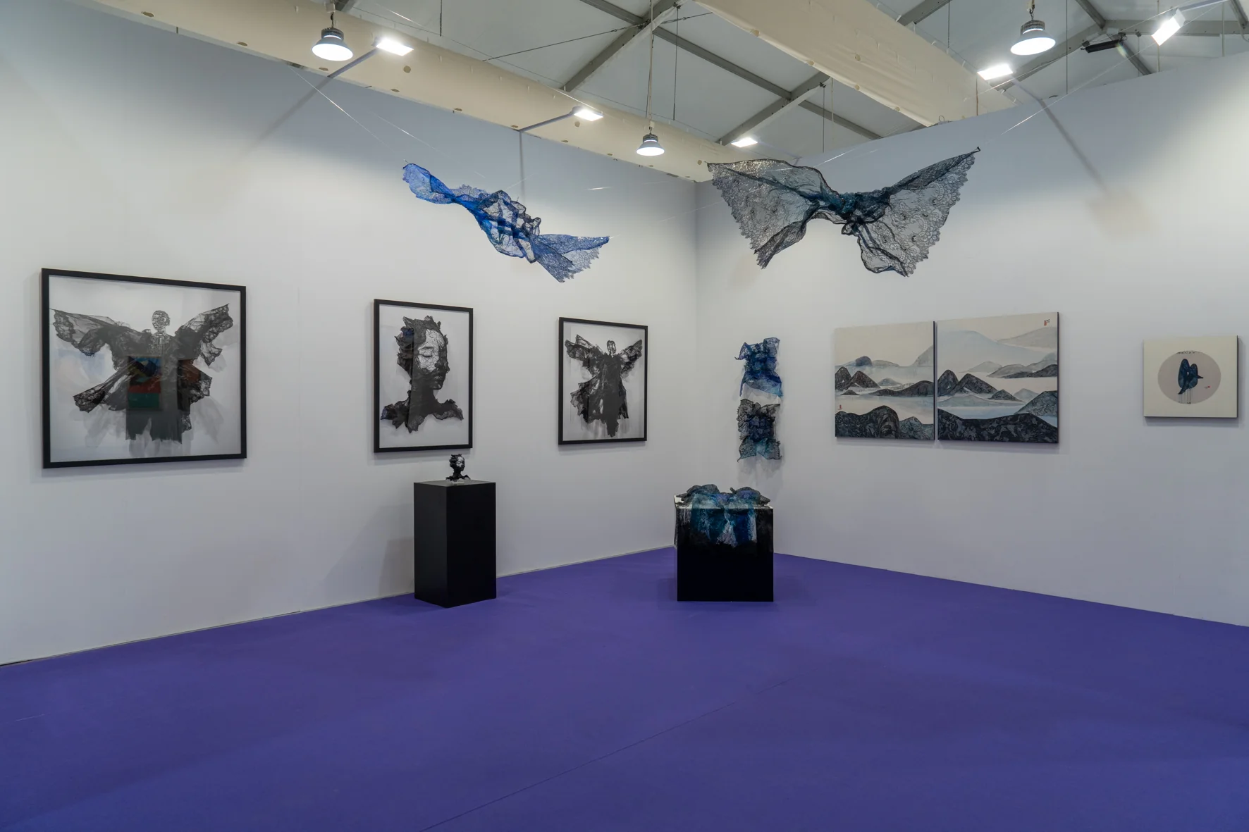 A gallery installation featuring two suspended, net-like sculptures in blue and black against a white backdrop.