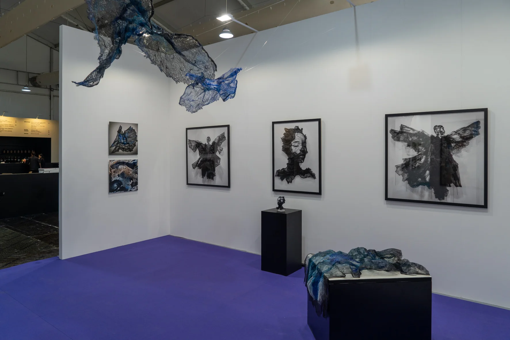 A sculptural arrangement of layered lace fabrics in deep blue and black tones, draped over a white rectangular base.